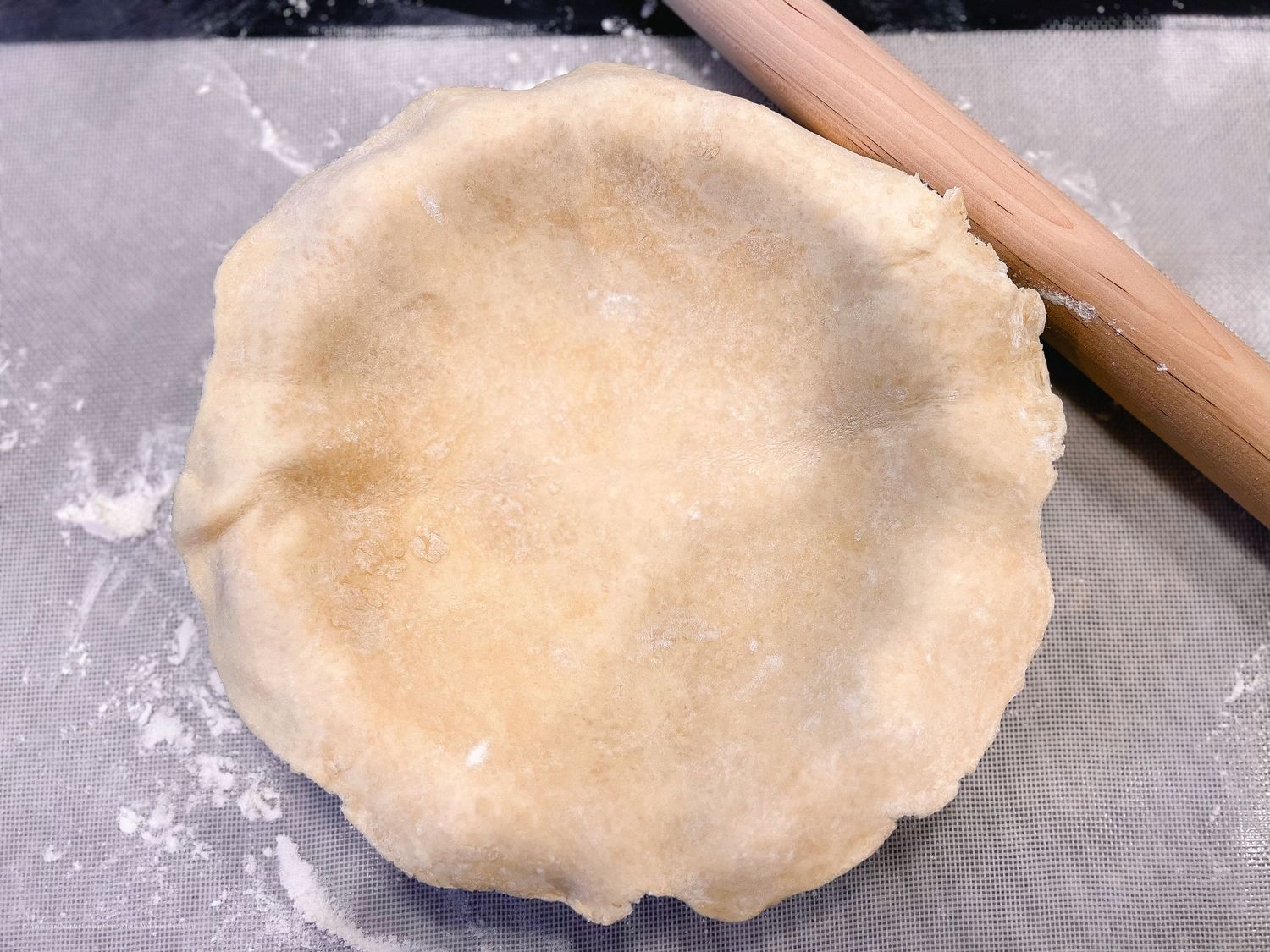 Rolling out pie dough on a floured surface with a wooden rolling pin.