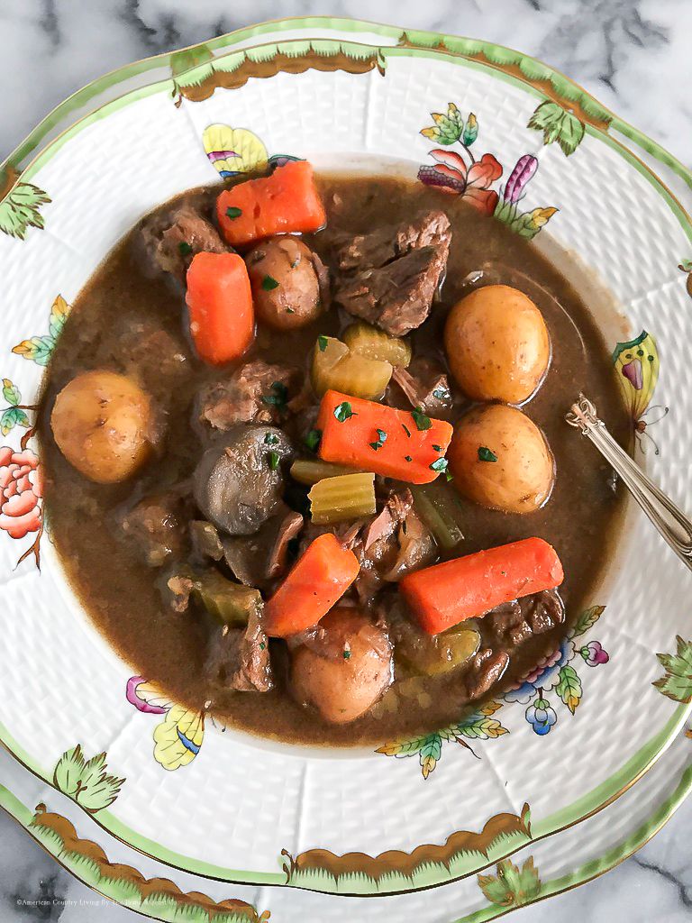 A hearty beef stew with tender carrots and potatoes simmered in rich brown gravy served in decorative china bowls.