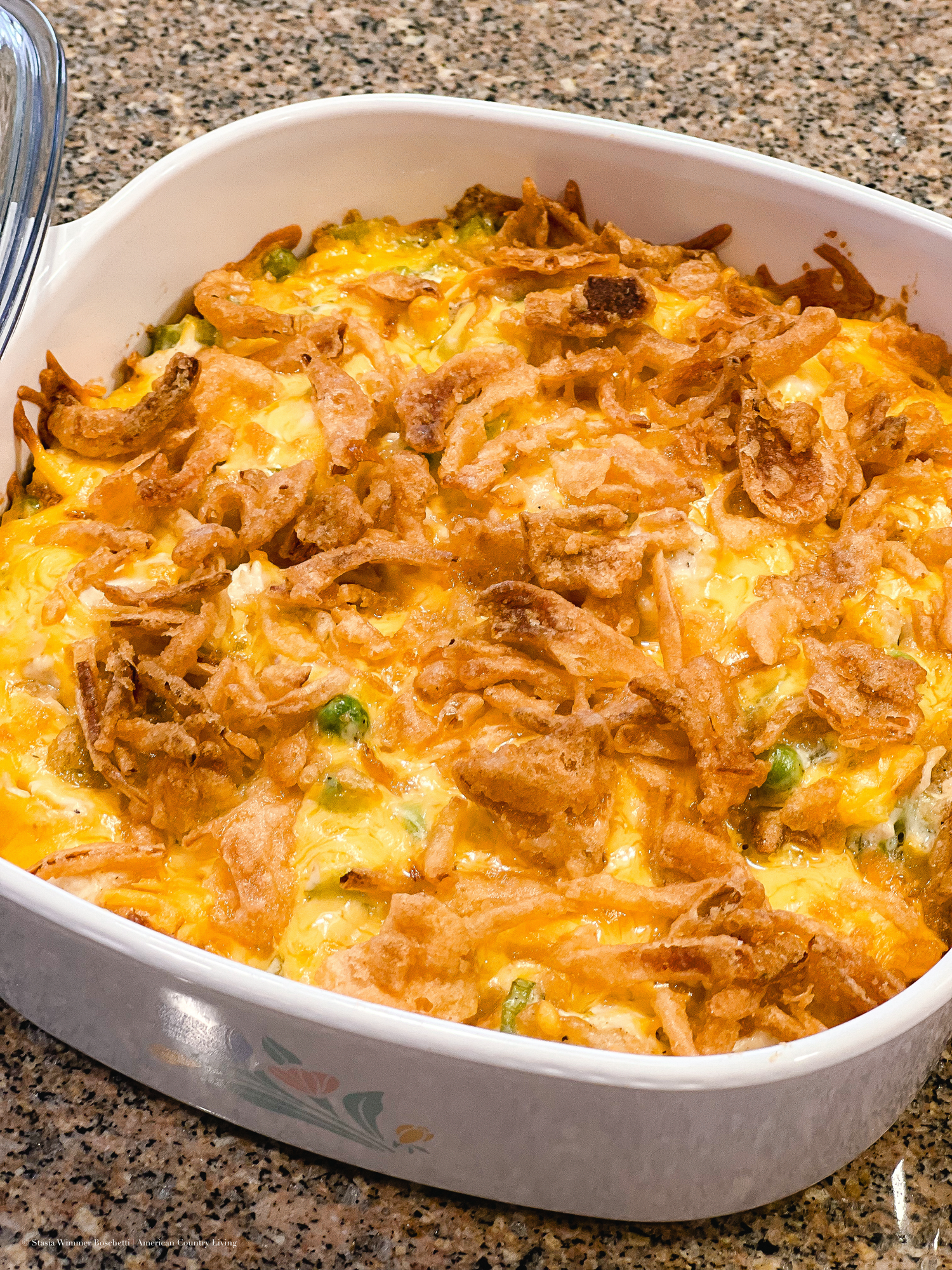 Golden cheesy green bean casserole topped with crispy fried onions baked in a white ceramic dish.