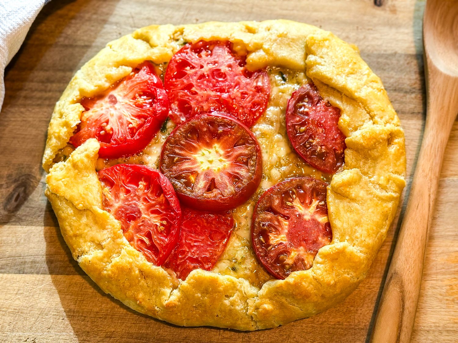Rustic tomato galette with sliced heirloom tomatoes on a flaky golden crust, served on a wooden cutting board.