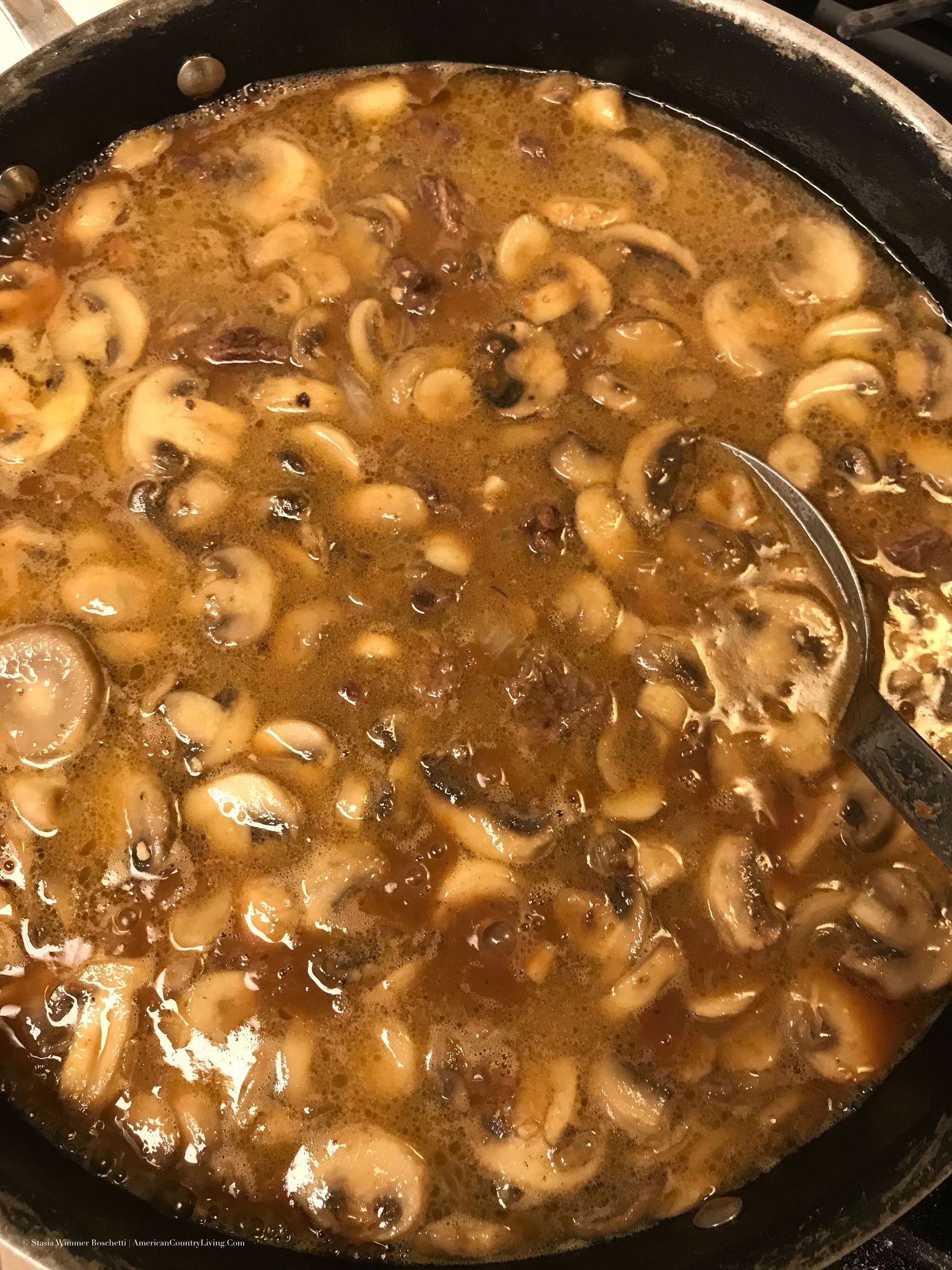 Cast iron skillet filled with sliced mushrooms simmering in a rich brown beef stroganoff sauce.