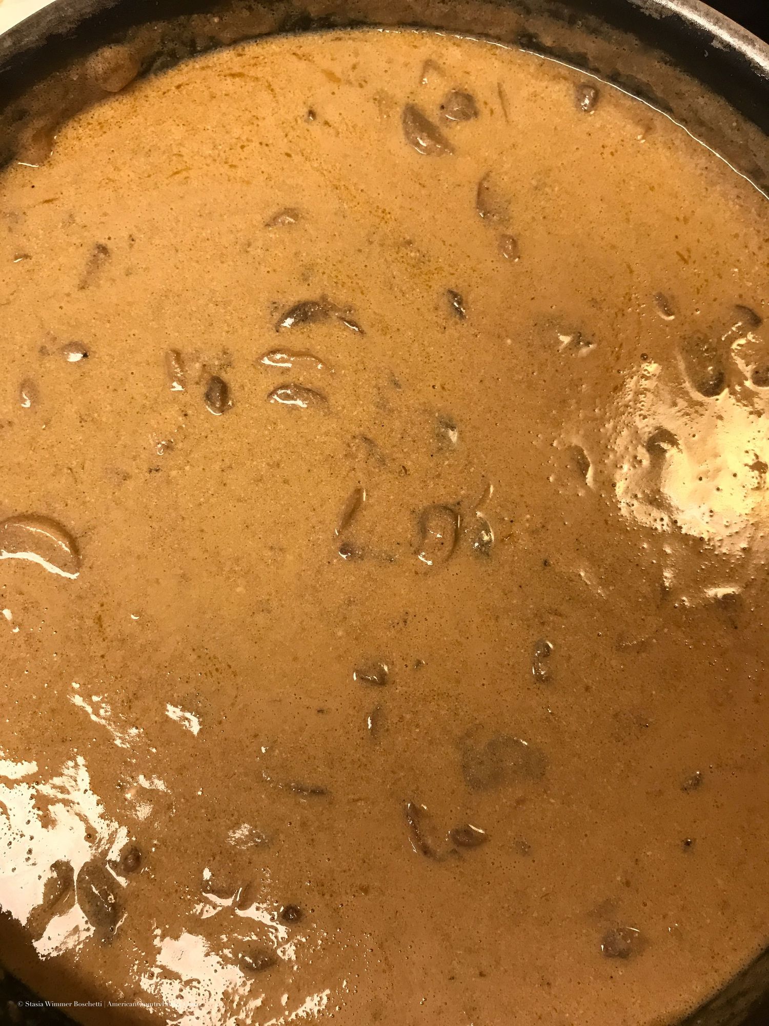 Rich golden-brown creamy stroganoff sauce bubbling in a cast iron skillet.