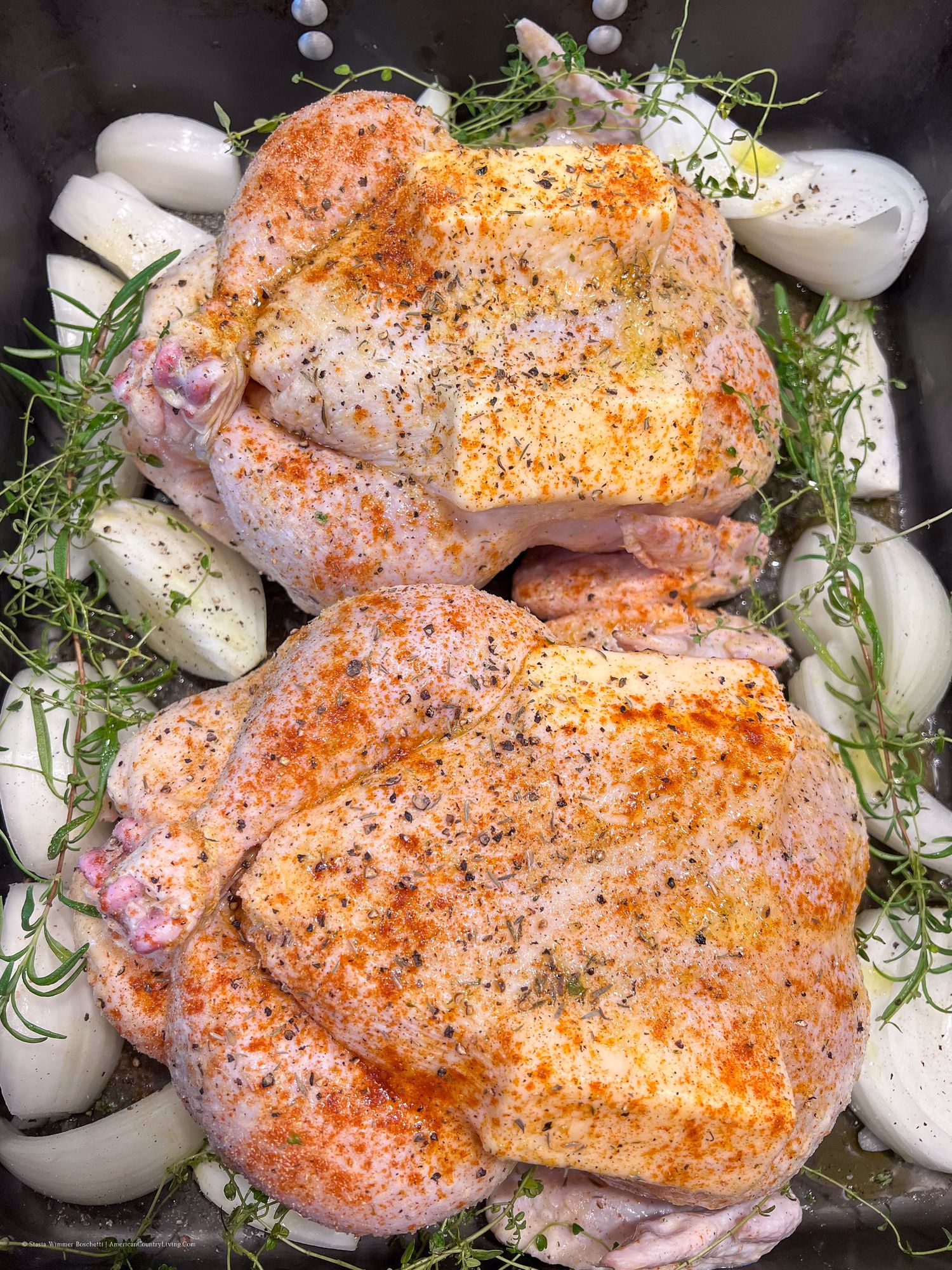 Fresh chicken thighs seasoned with spices and arranged with onions and herbs before cooking.