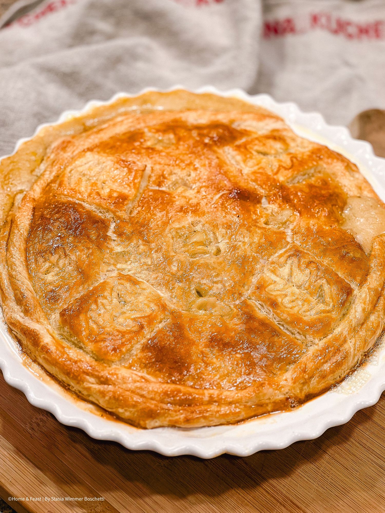 Golden brown pot pie with flaky pastry crust baked in a white ceramic dish.