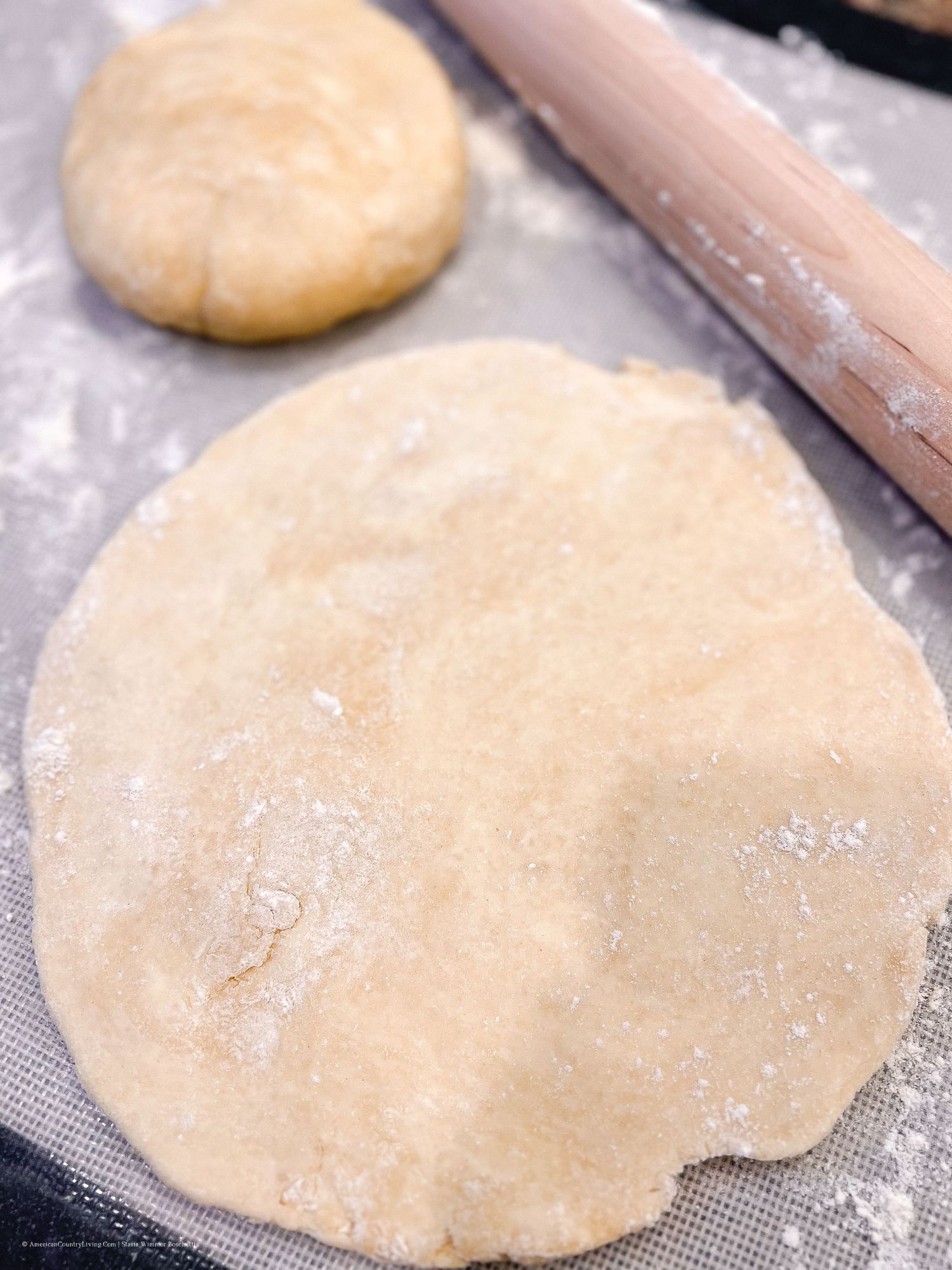 Raw pie dough being flattened with a rolling pin on a non-stick surface.