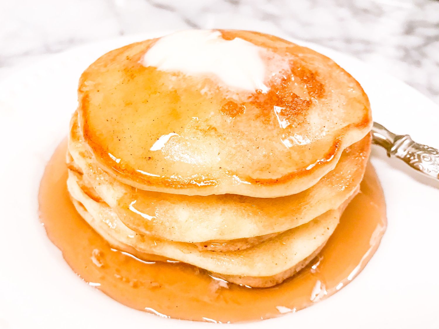 Stack of golden pancakes drizzled with maple syrup on a white plate.