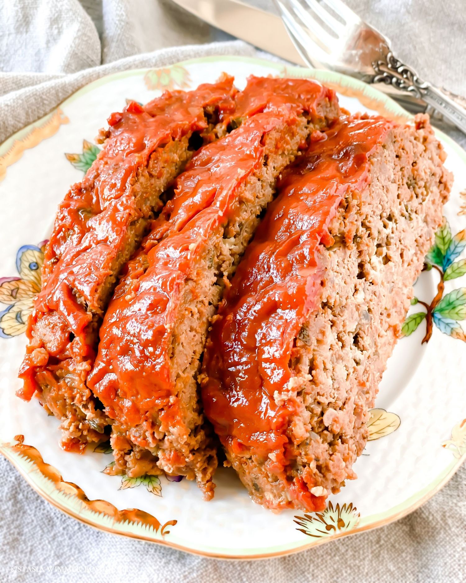Glazed meatloaf slices arranged on a vintage floral plate with garnish.