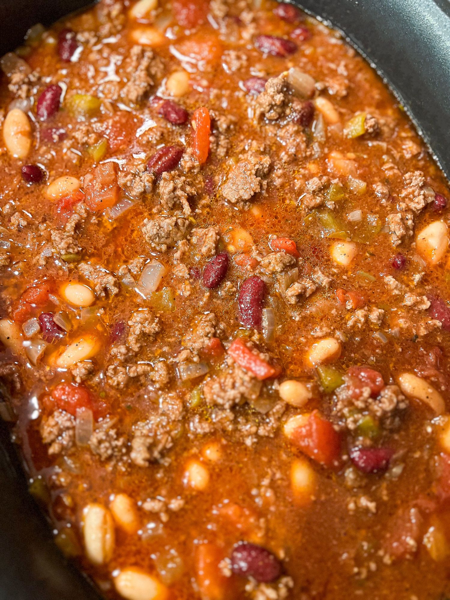 Hearty chili with ground beef, beans, and tomatoes simmering in a black pan.