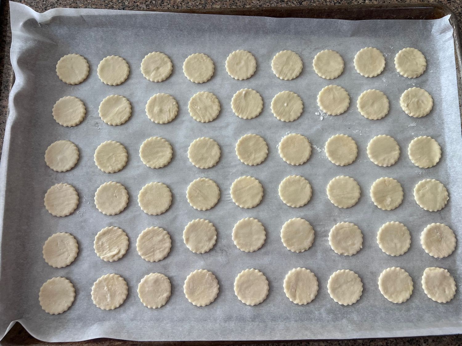 Rows of small round pastry circles arranged on parchment-lined baking sheet.