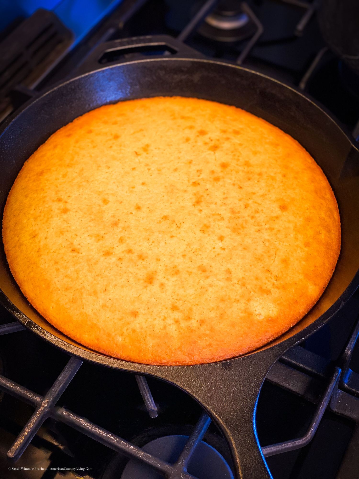 Golden cornbread baked in a cast iron skillet on a gas stovetop, perfectly risen with a crispy edges.