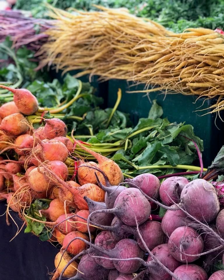 Colorful bundles of fresh beets and golden carrots displayed at a farmers market stand.