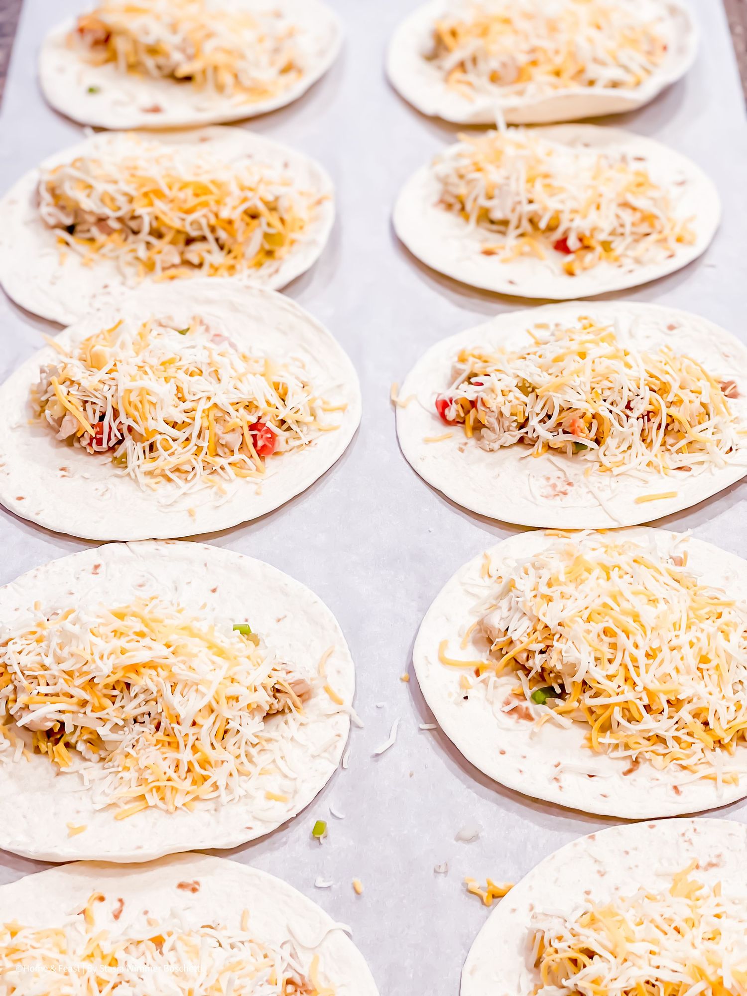 Tortillas topped with shredded chicken and cheese ready for baking.