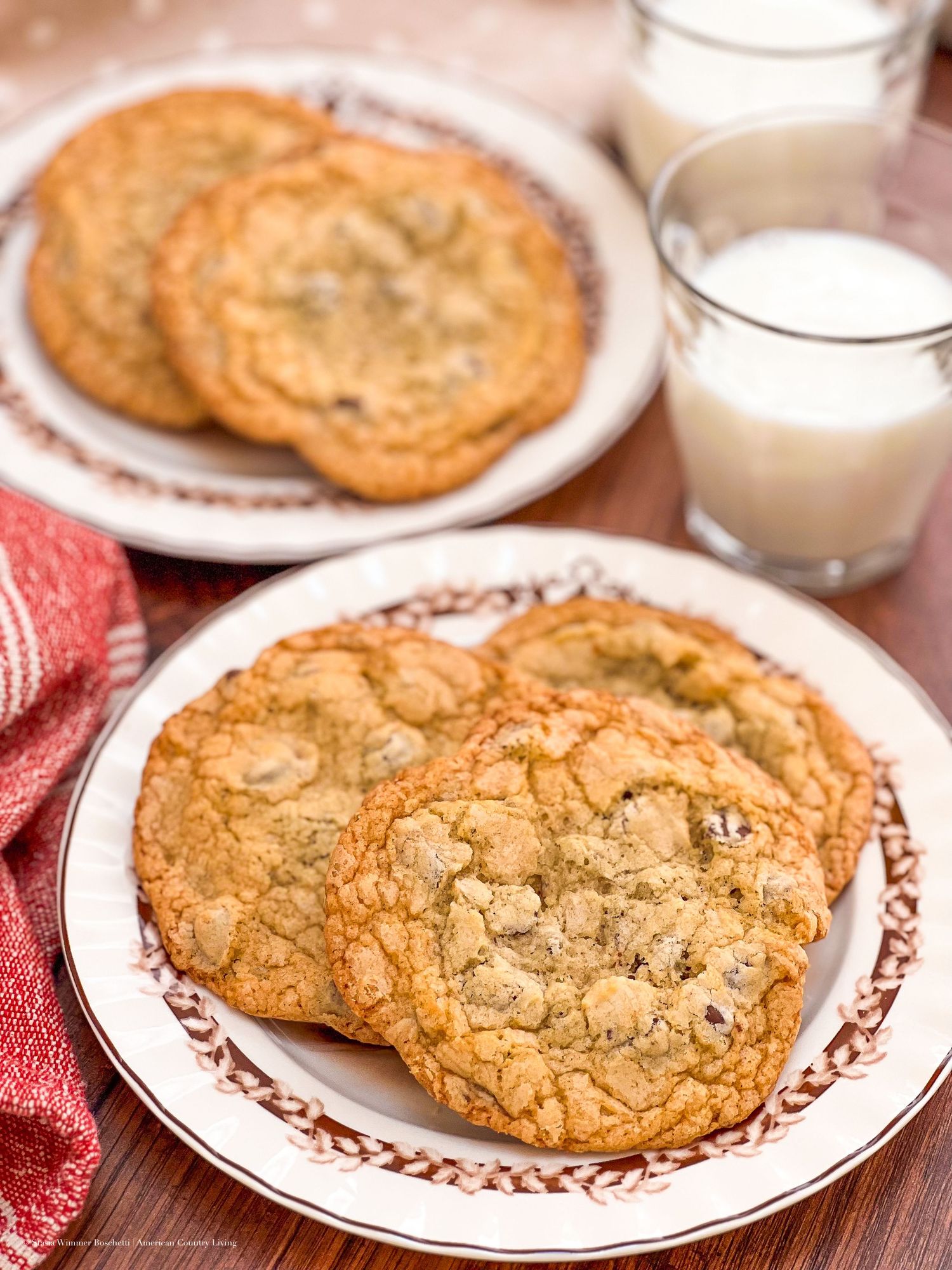 Freshly baked chocolate chip cookies on decorative plates with glasses of cold milk.