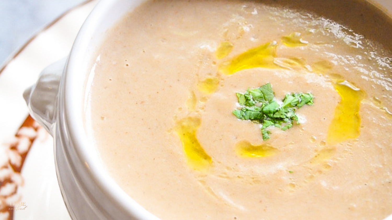 Close-up of cream colored soup with green herb garnish and yellow oil drizzle.
