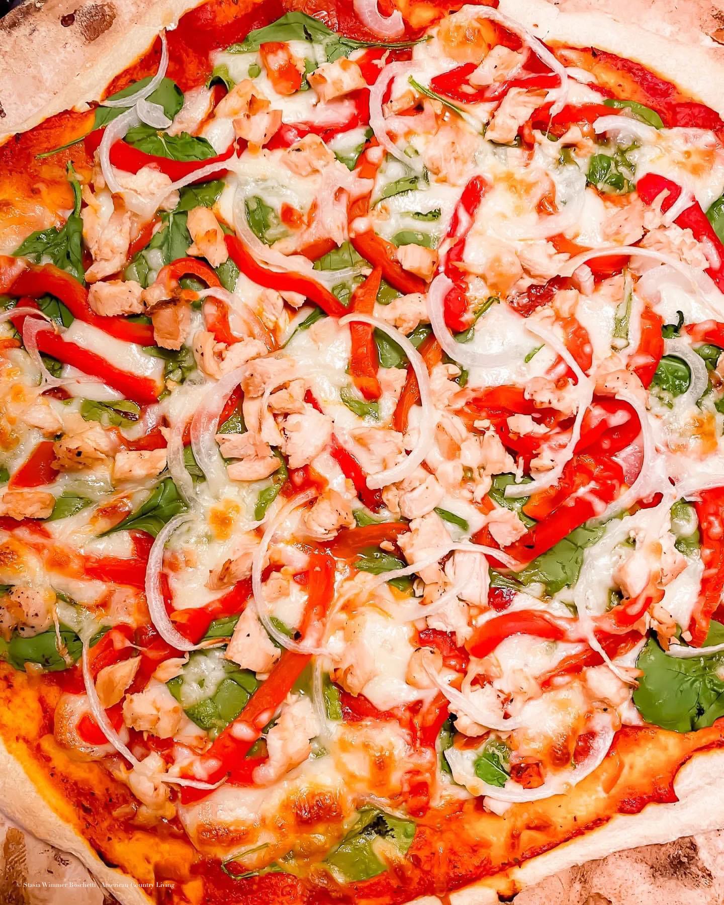 Fresh pizza topped with melted mozzarella, red peppers, red onions, spinach, and seasoned chicken on tomato sauce.