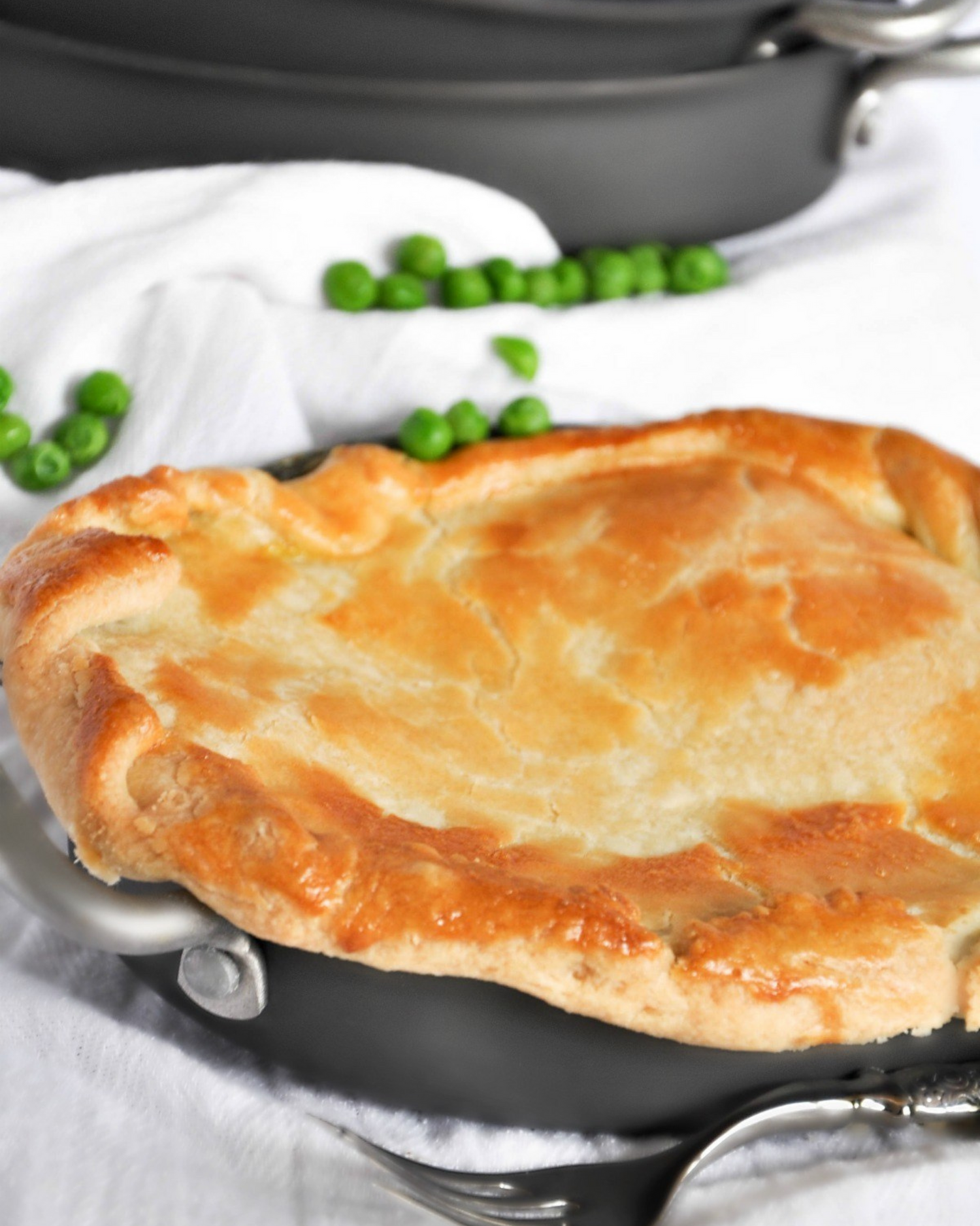 Golden brown chicken pot pie with flaky crust and peas on the side.