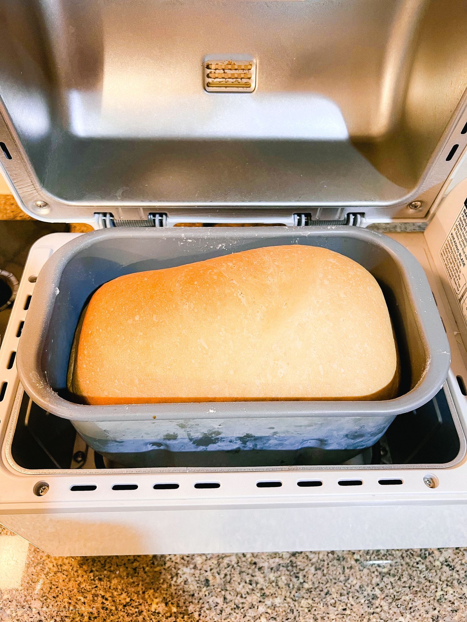 White bread loaf baking in a bread machine with stainless steel pan.