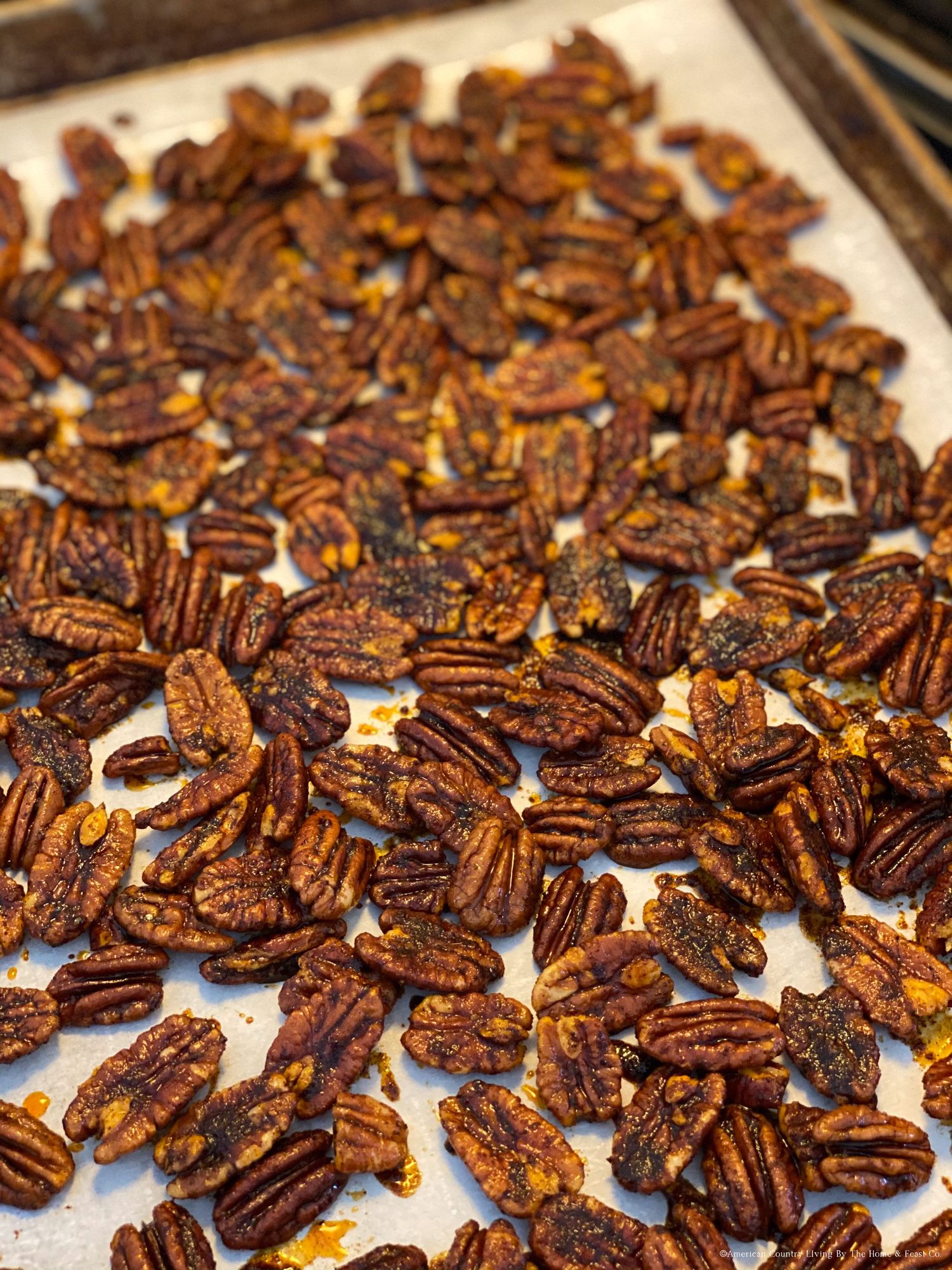 Freshly roasted pecans spread out on a baking sheet with spices and seasonings.