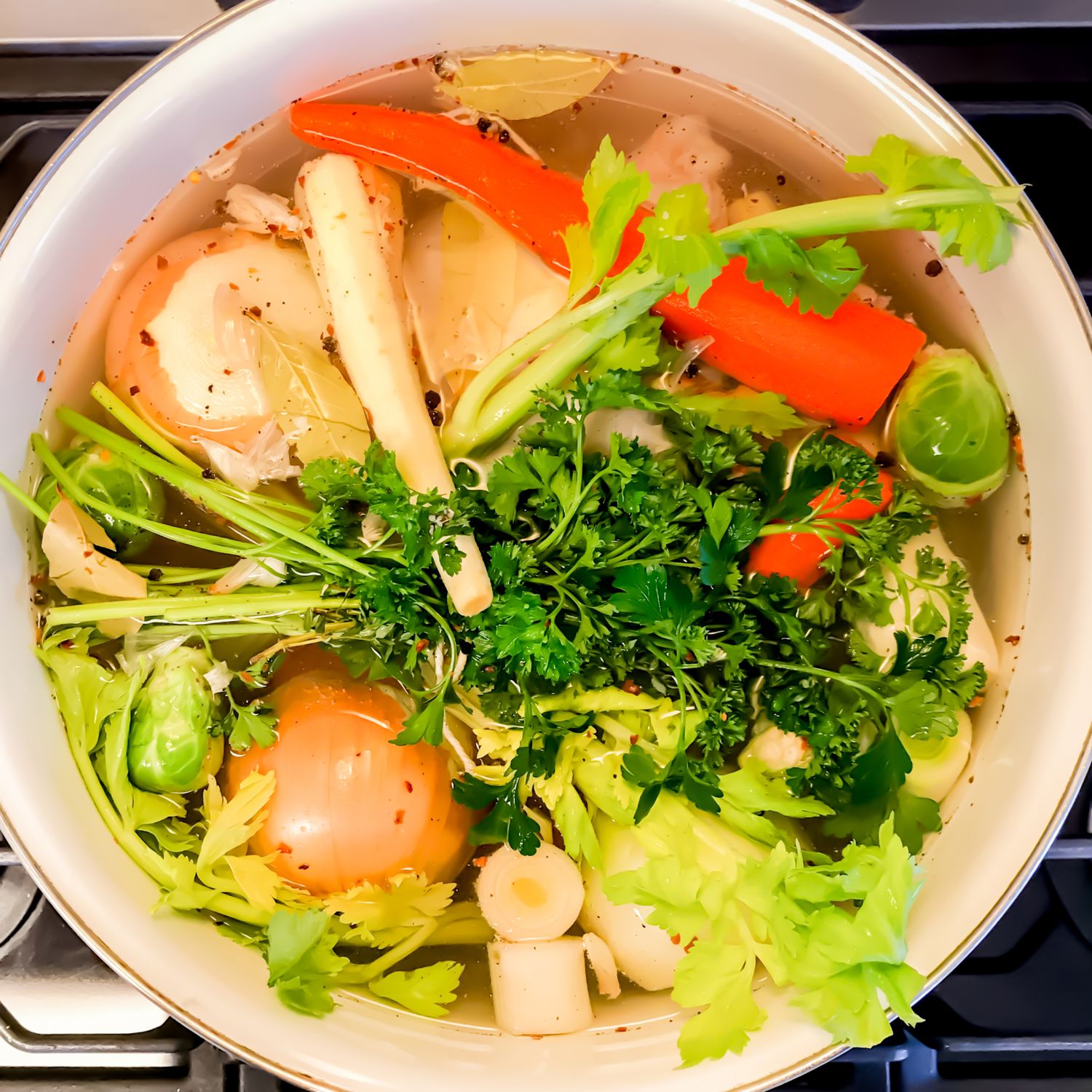 Vegetable soup with carrots, celery, and herbs cooking in a white enamel pot.