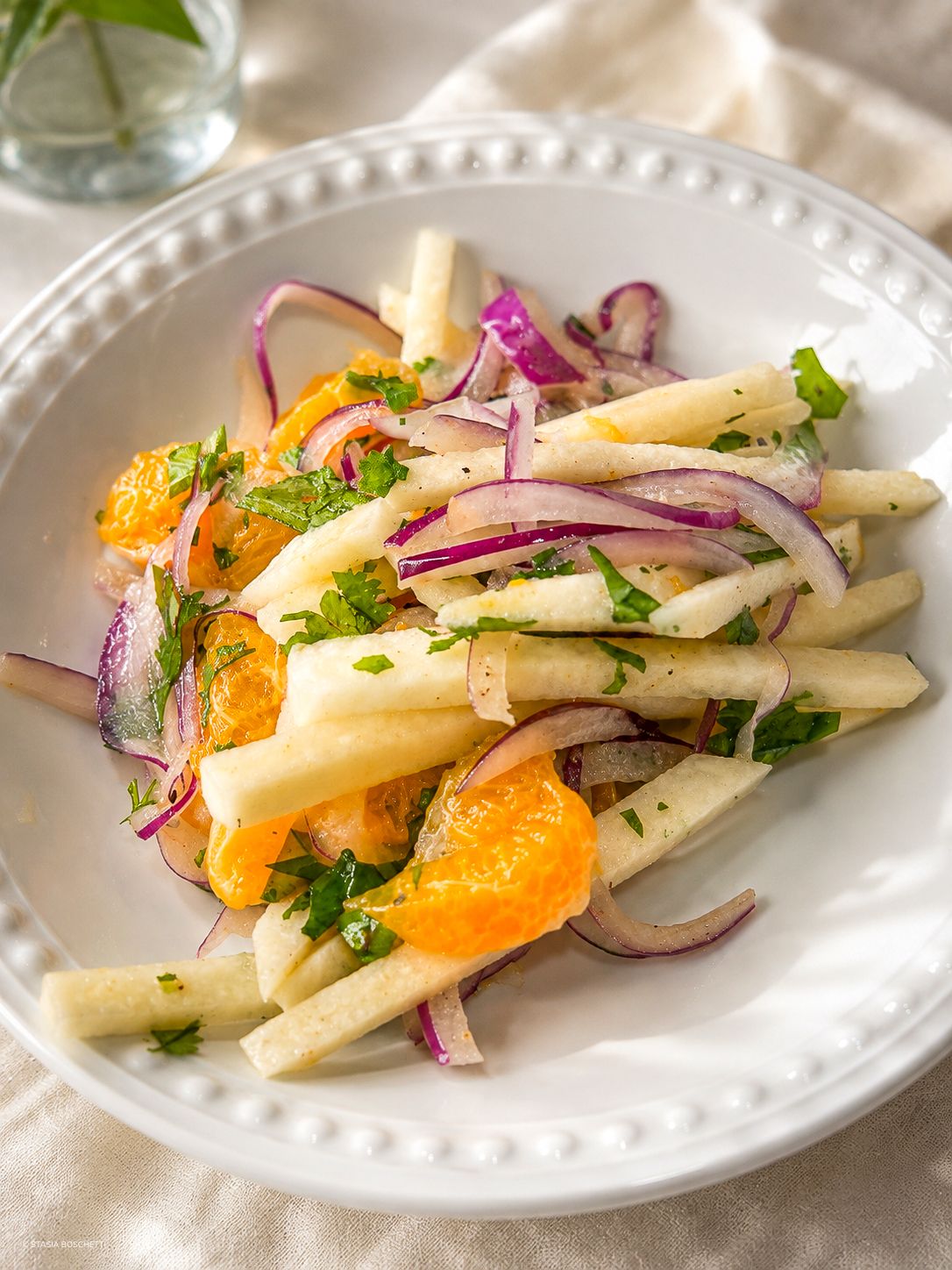 White asparagus salad with mandarin oranges, red onion, and fresh herbs on a white plate.