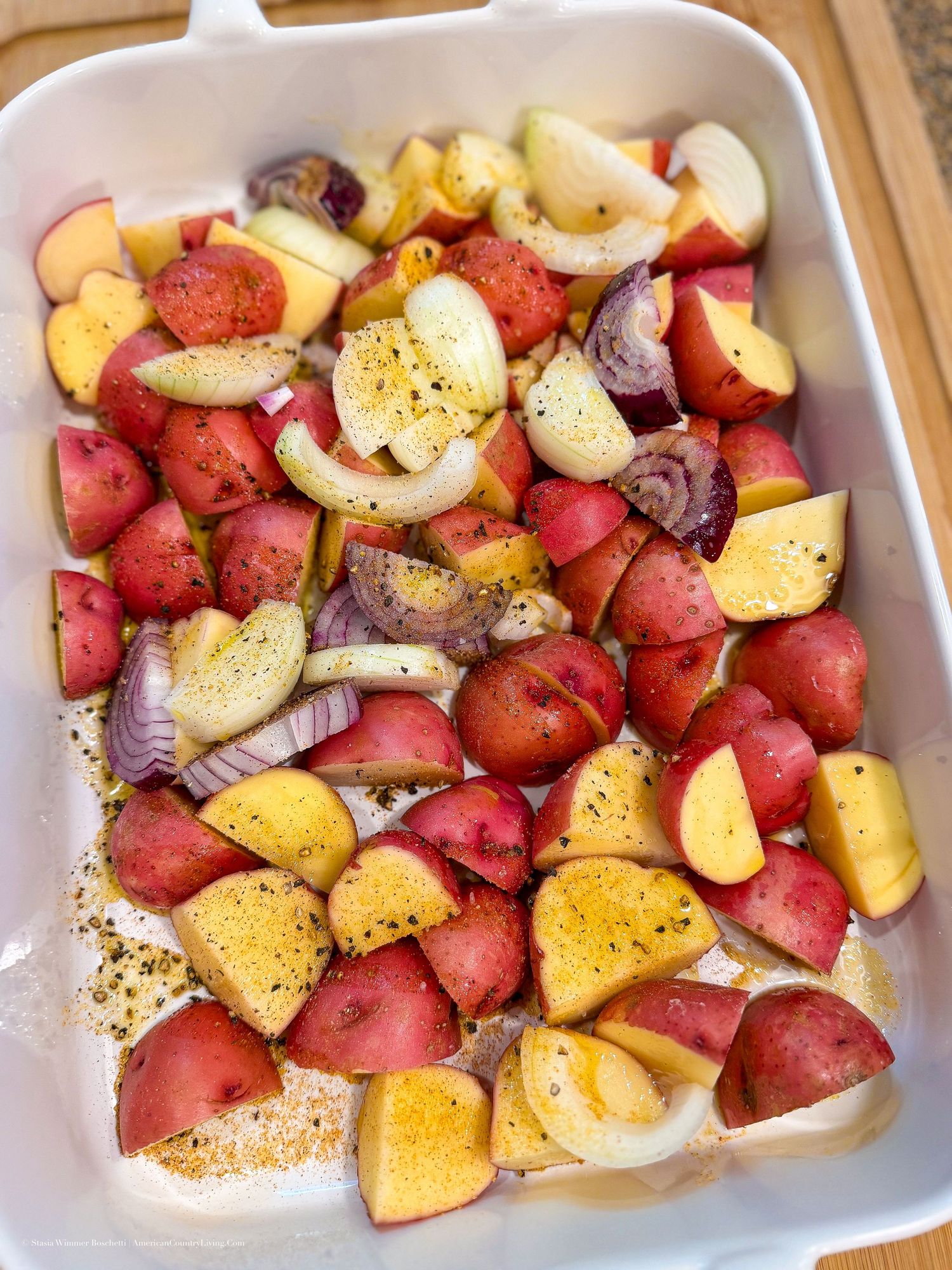 Chopped red potatoes and onions seasoned with pepper in a white baking dish, ready for roasting.