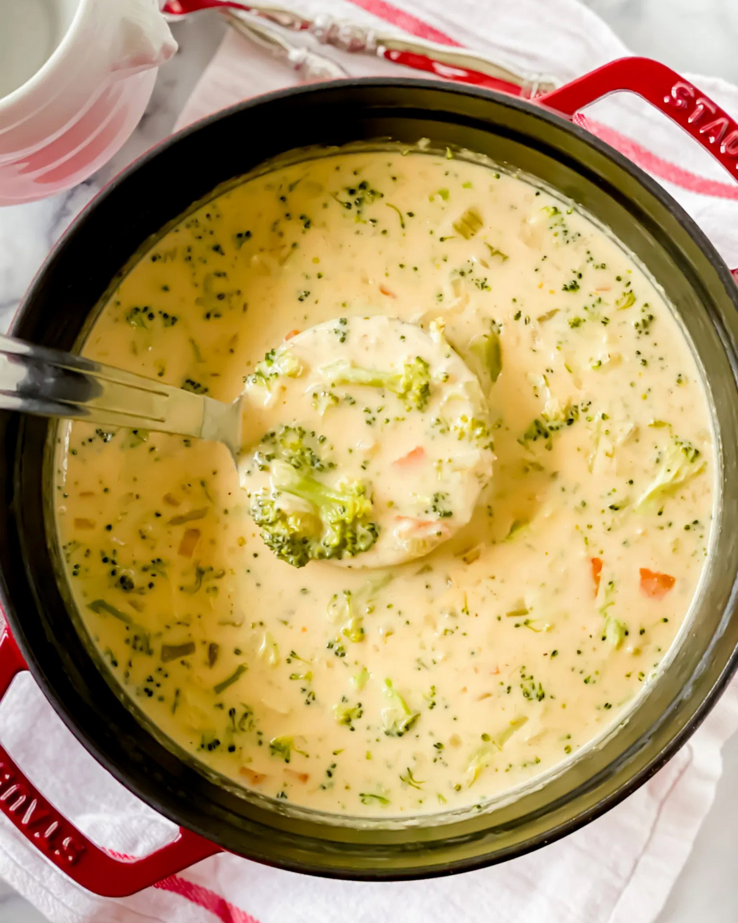 Homemade cream of broccoli soup with herbs in a red cooking pot.