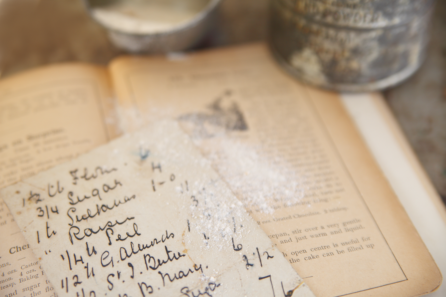 Vintage handwritten recipe book open on a rustic surface dusted with flour, with antique measuring cups in the background.
