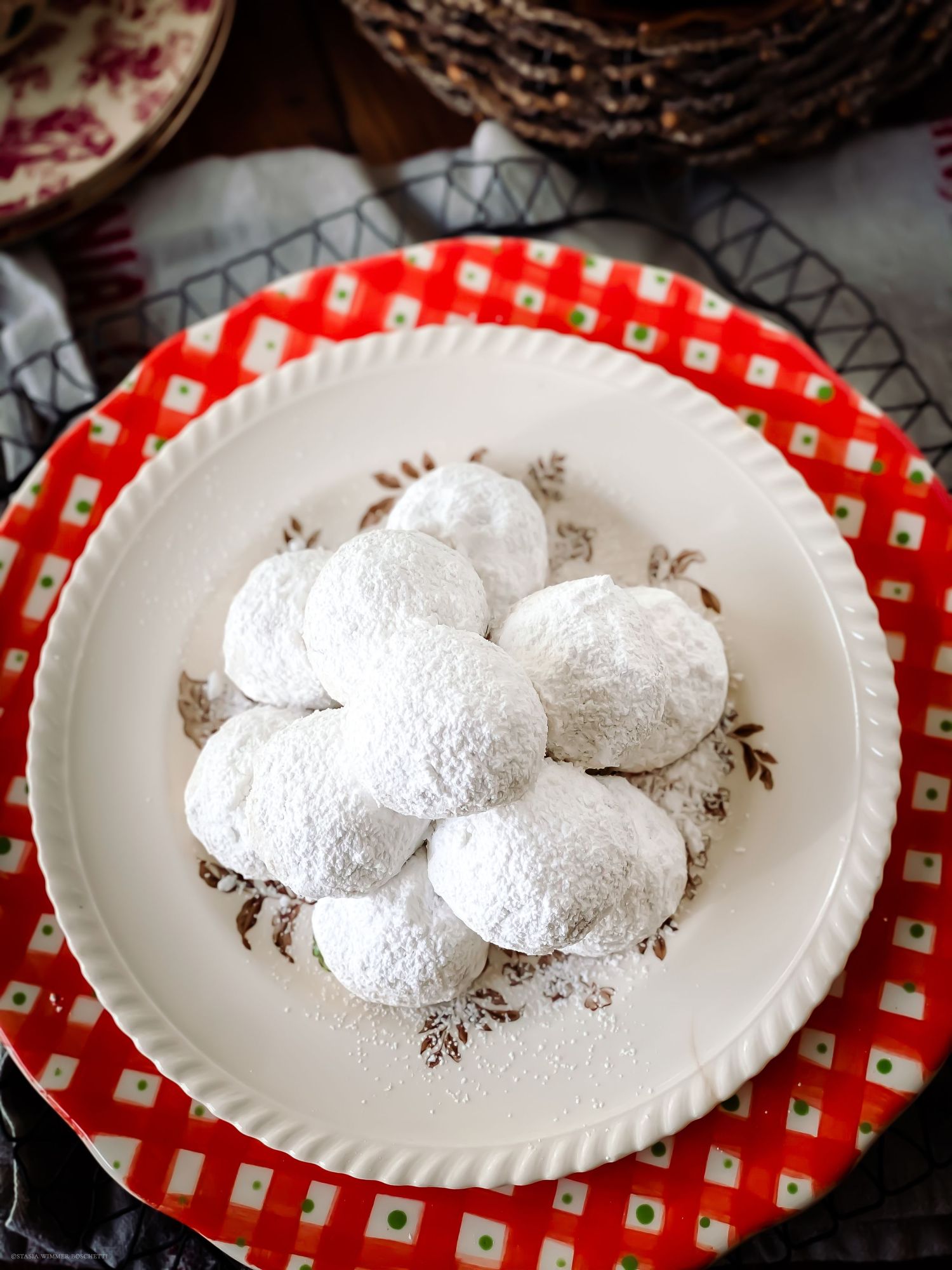 Powdered sugar coated Russian tea cakes on a decorative plate with red and white checkered placemat.