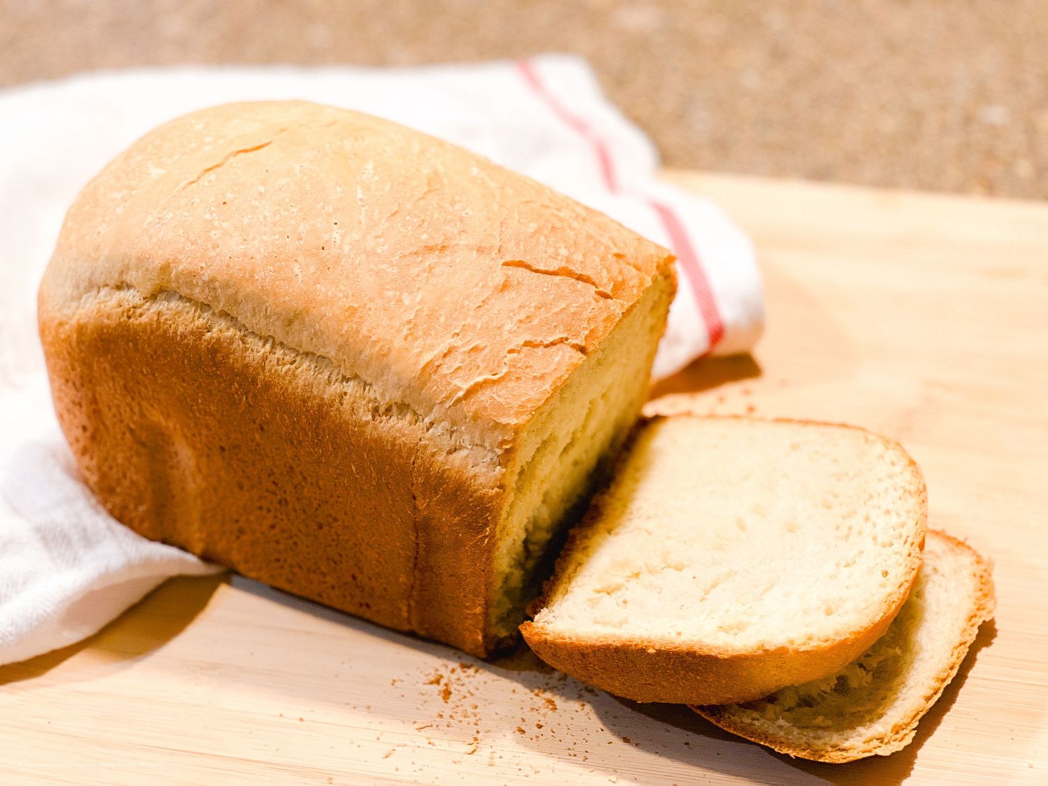 Freshly baked golden loaf of bread sliced on a wooden cutting board.