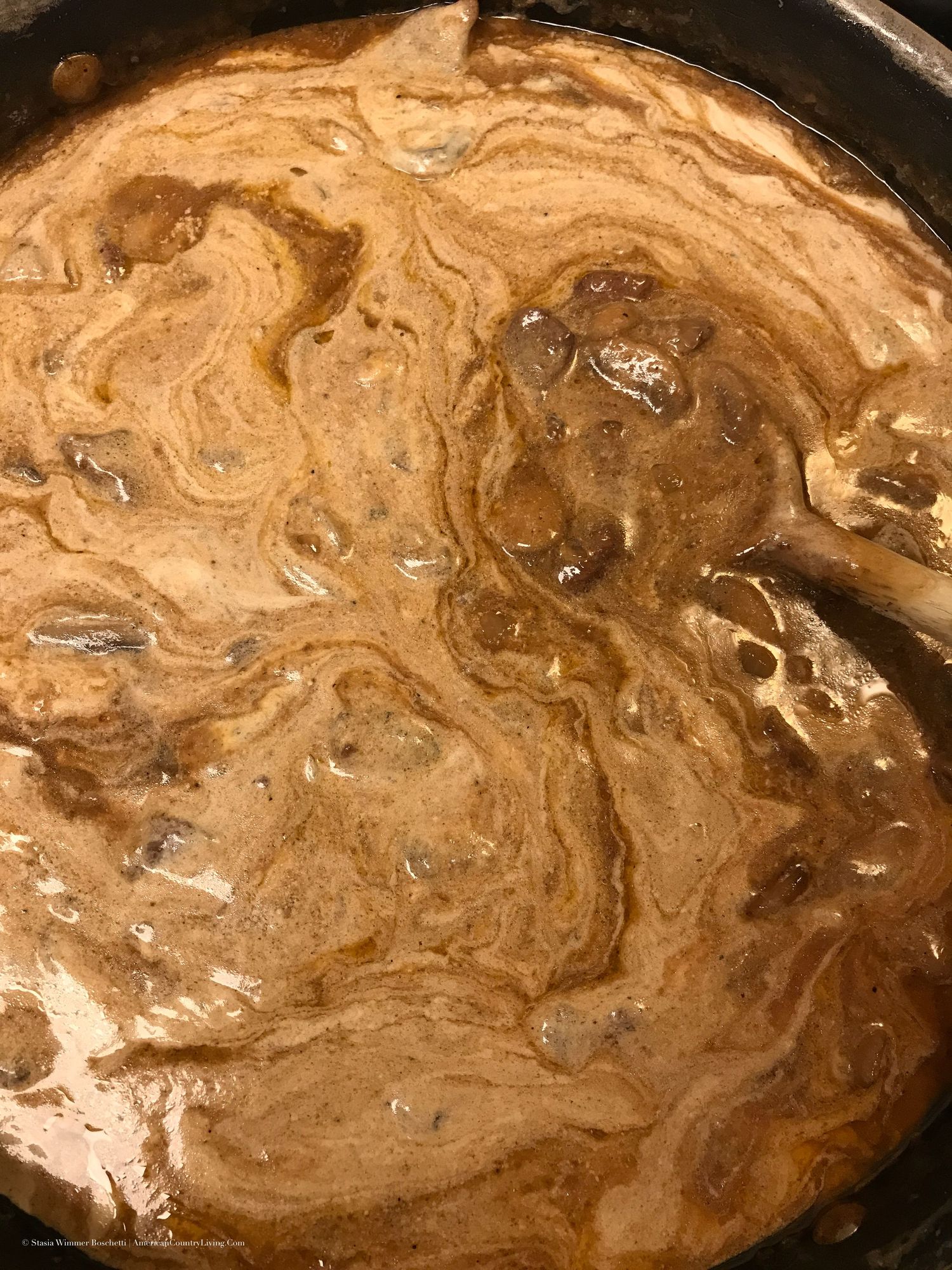 Creamy brown mushroom stroganoff sauce being stirred in a cast iron skillet.