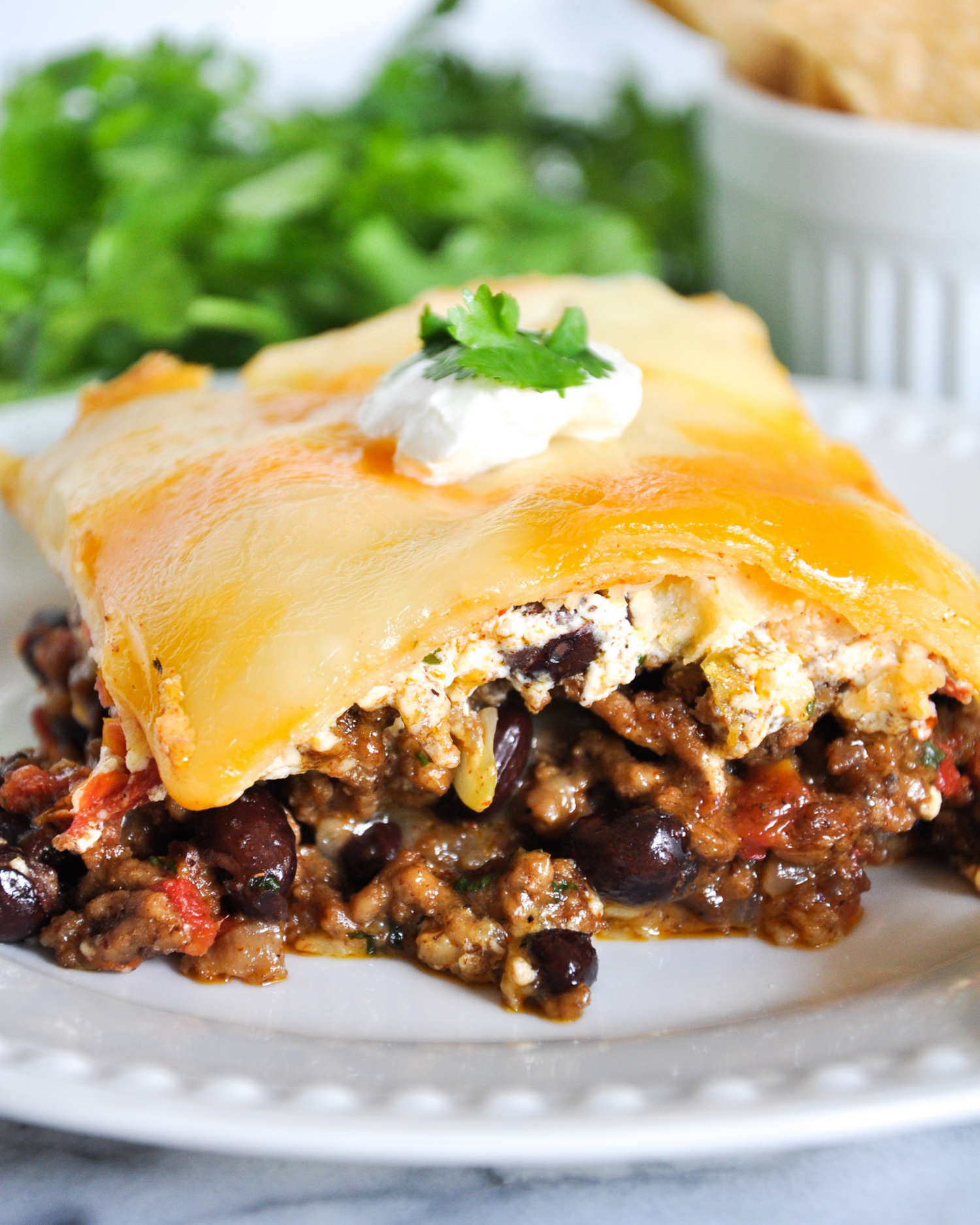 Baked Mexican casserole with melted cheddar cheese and black beans served on a white plate.