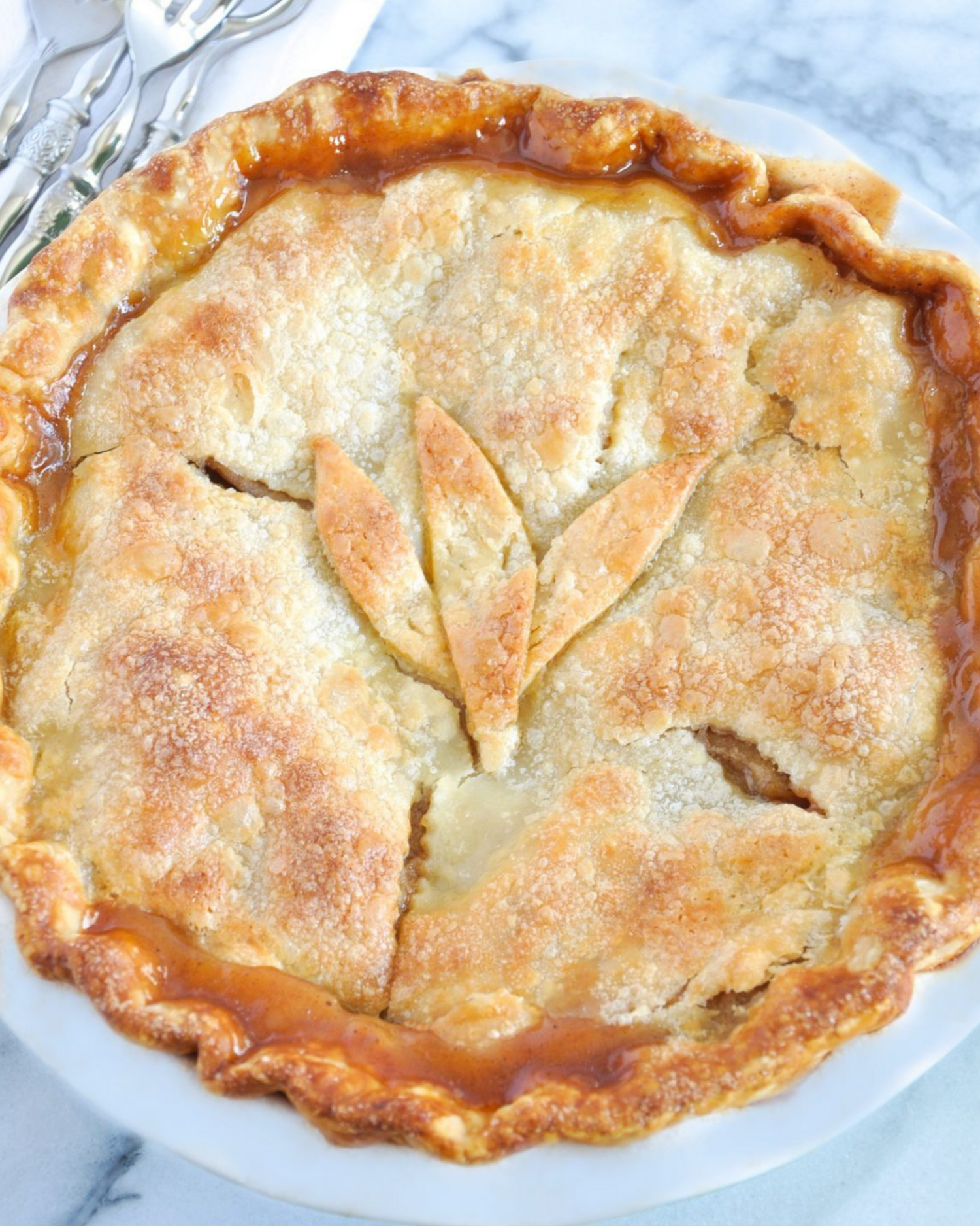 Golden brown apple pie with flaky crust and vents on marble surface.