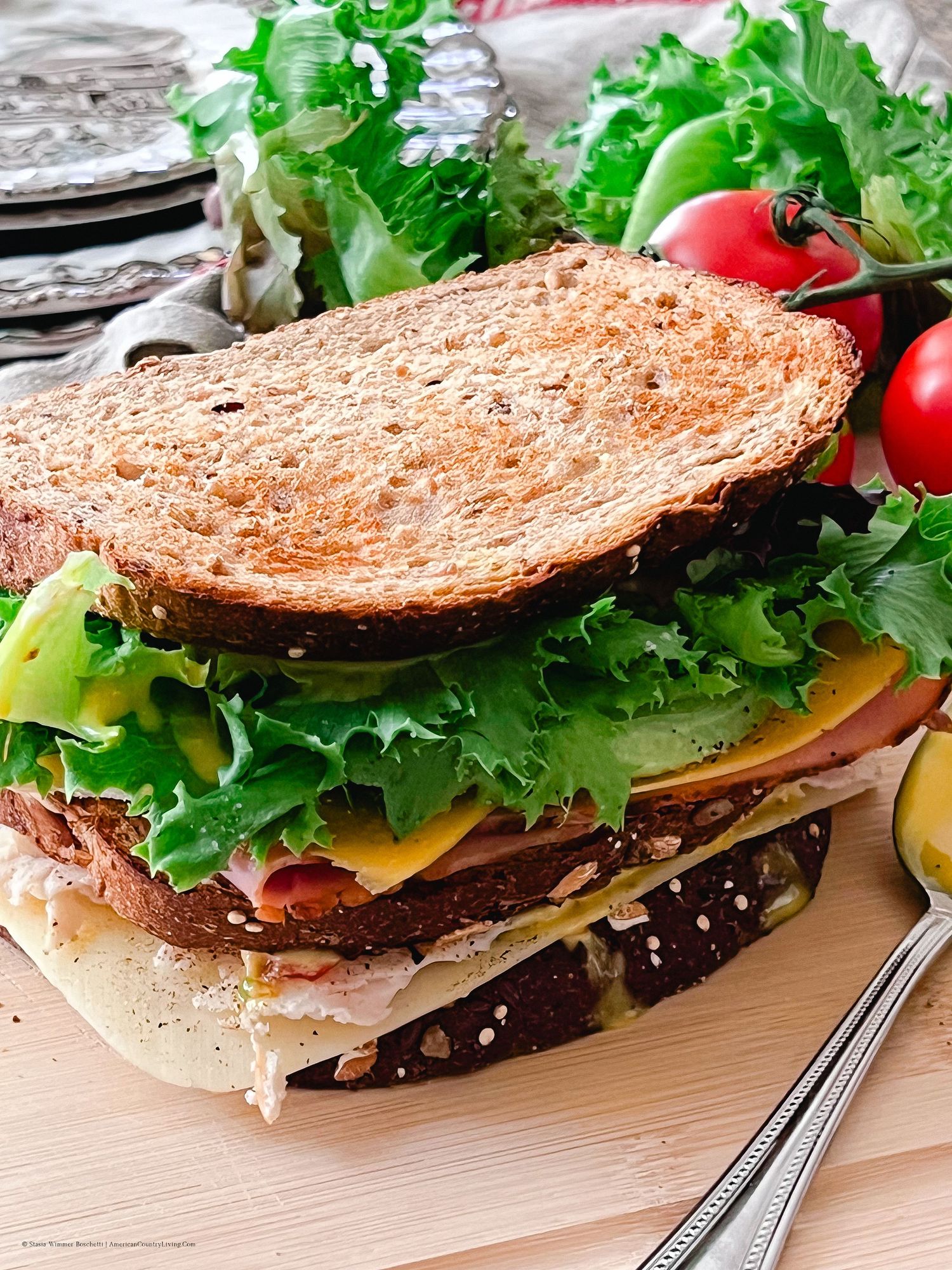 Fresh deli sandwich with lettuce, cheese and meat on wooden board with tomatoes.