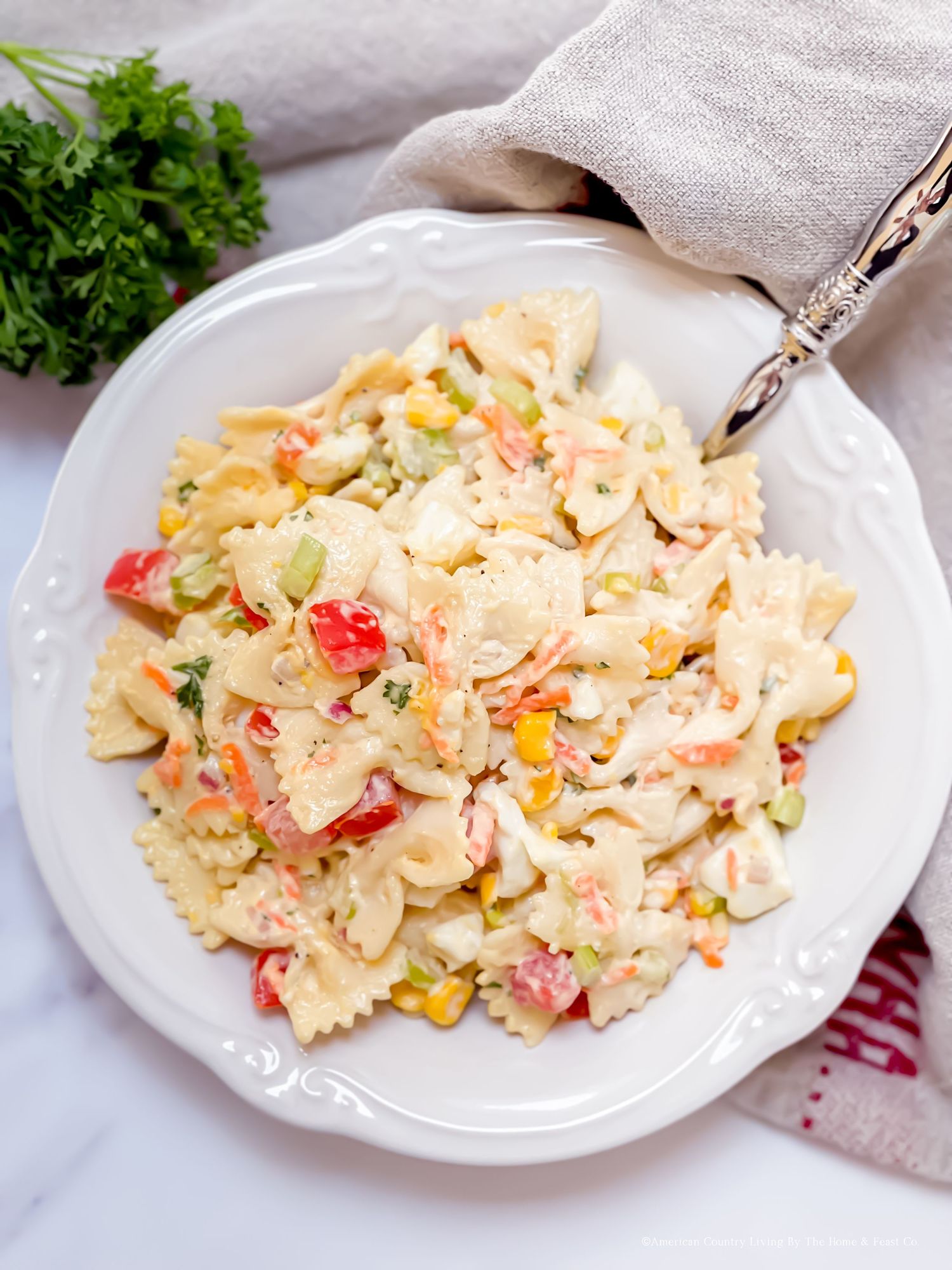 Creamy pasta salad with fresh vegetables garnished with herbs.