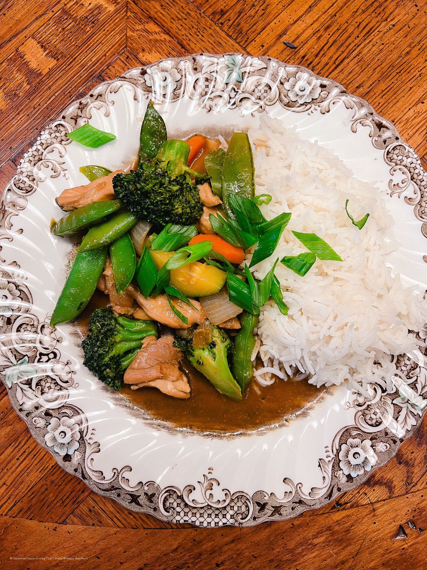 Stir fried chicken with vegetables and rice presented on an elegant white plate with patterned edges.