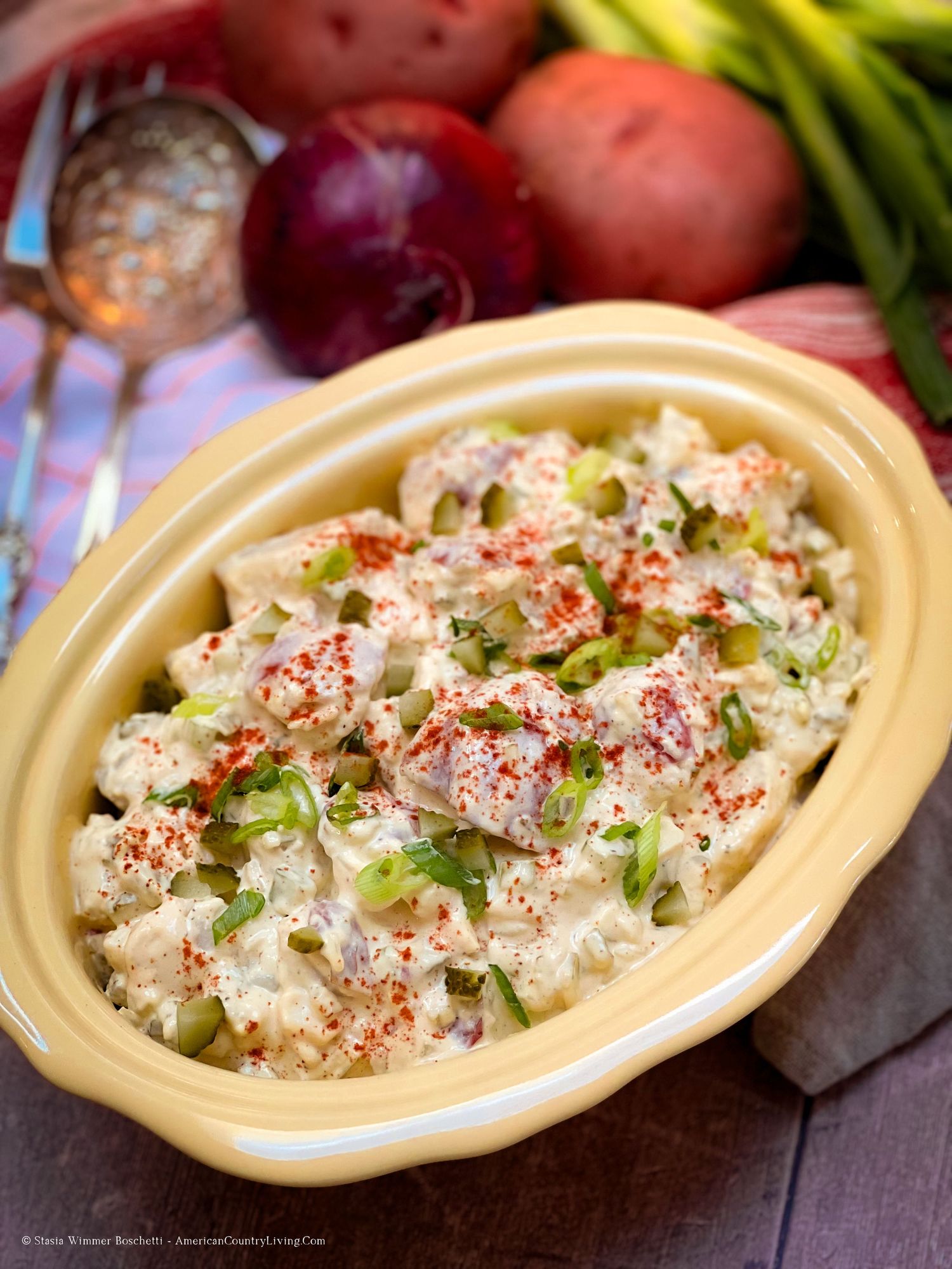 Homestyle potato salad topped with paprika and green onions in a yellow serving dish.