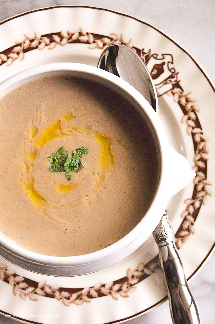 Creamy mushroom soup garnished with fresh herbs and olive oil drizzle, served in a white bowl on an elegant plate.