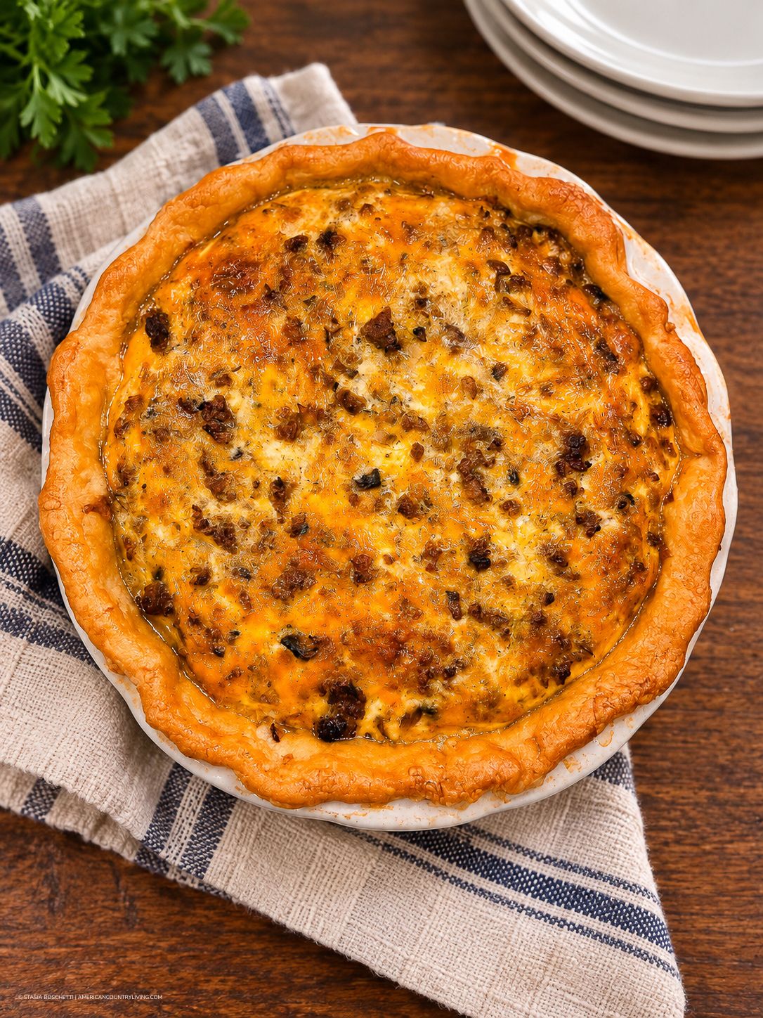 Golden-crusted quiche with sausage and melted cheese filling in a white pie dish on a striped cloth.
