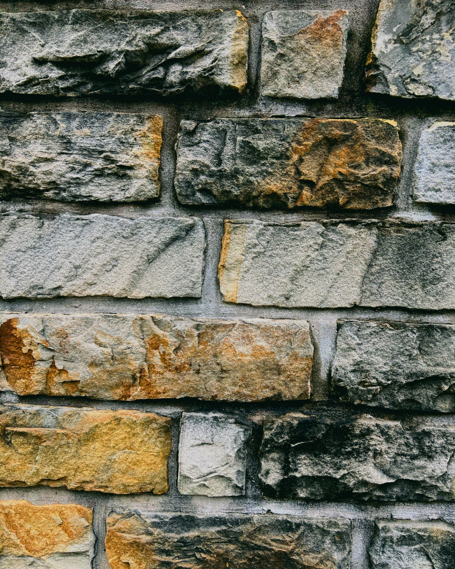 Close-up texture of weathered stone wall with gray and orange tones showing age and character.