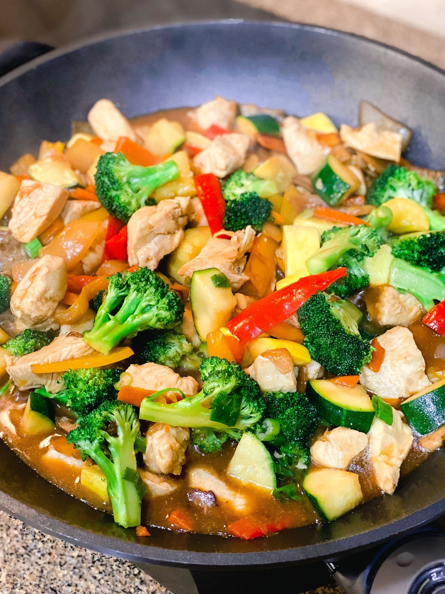 Sizzling chicken stir fry with fresh vegetables and sauce cooking in a large black skillet.