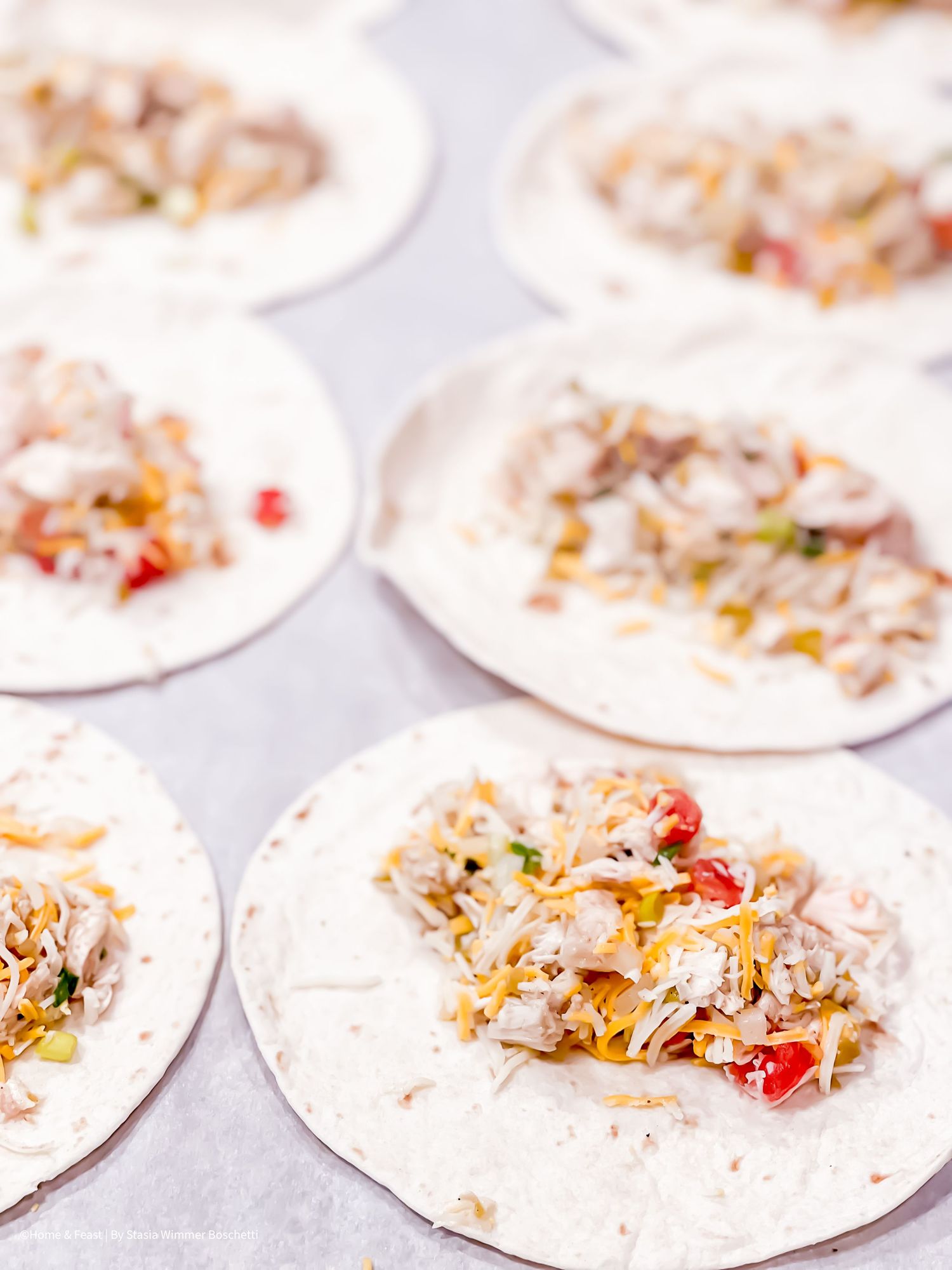 Multiple flour tortillas covered with melted cheese and toppings laid out for preparation.