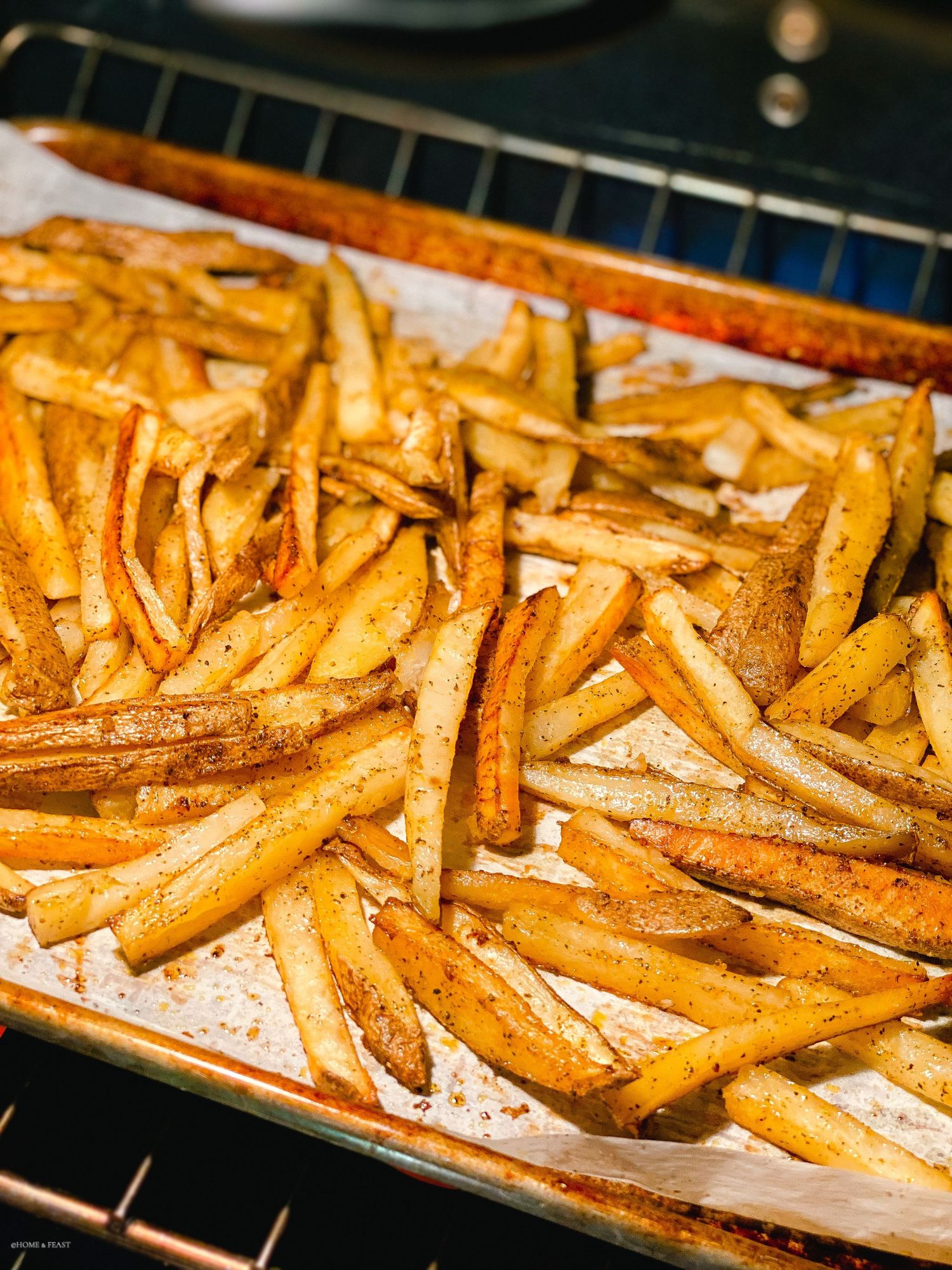 Golden brown french fries spread evenly on a baking sheet in the oven.