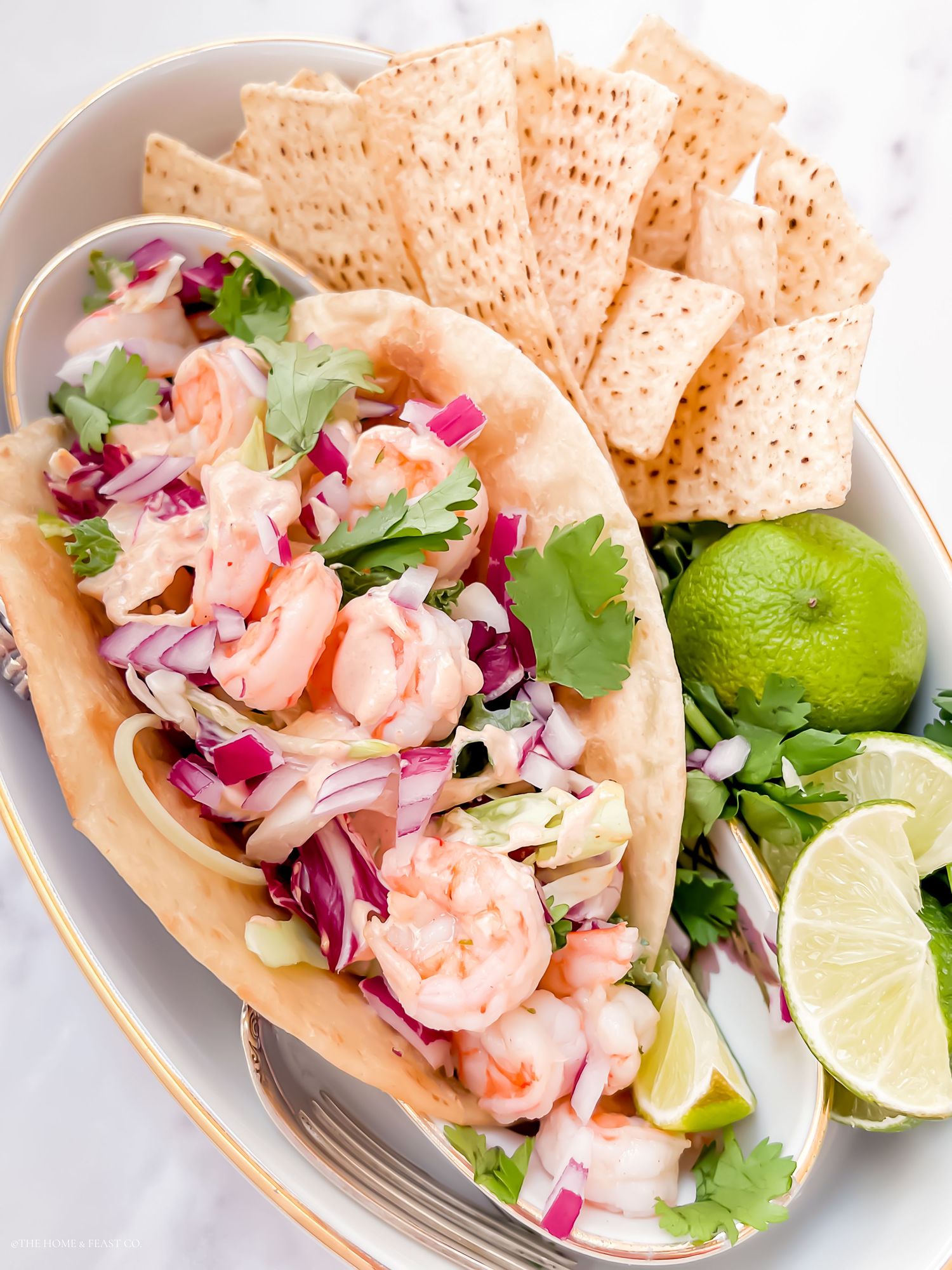 Fresh shrimp tacos topped with cabbage slaw and cilantro served on white plates with tortilla chips.