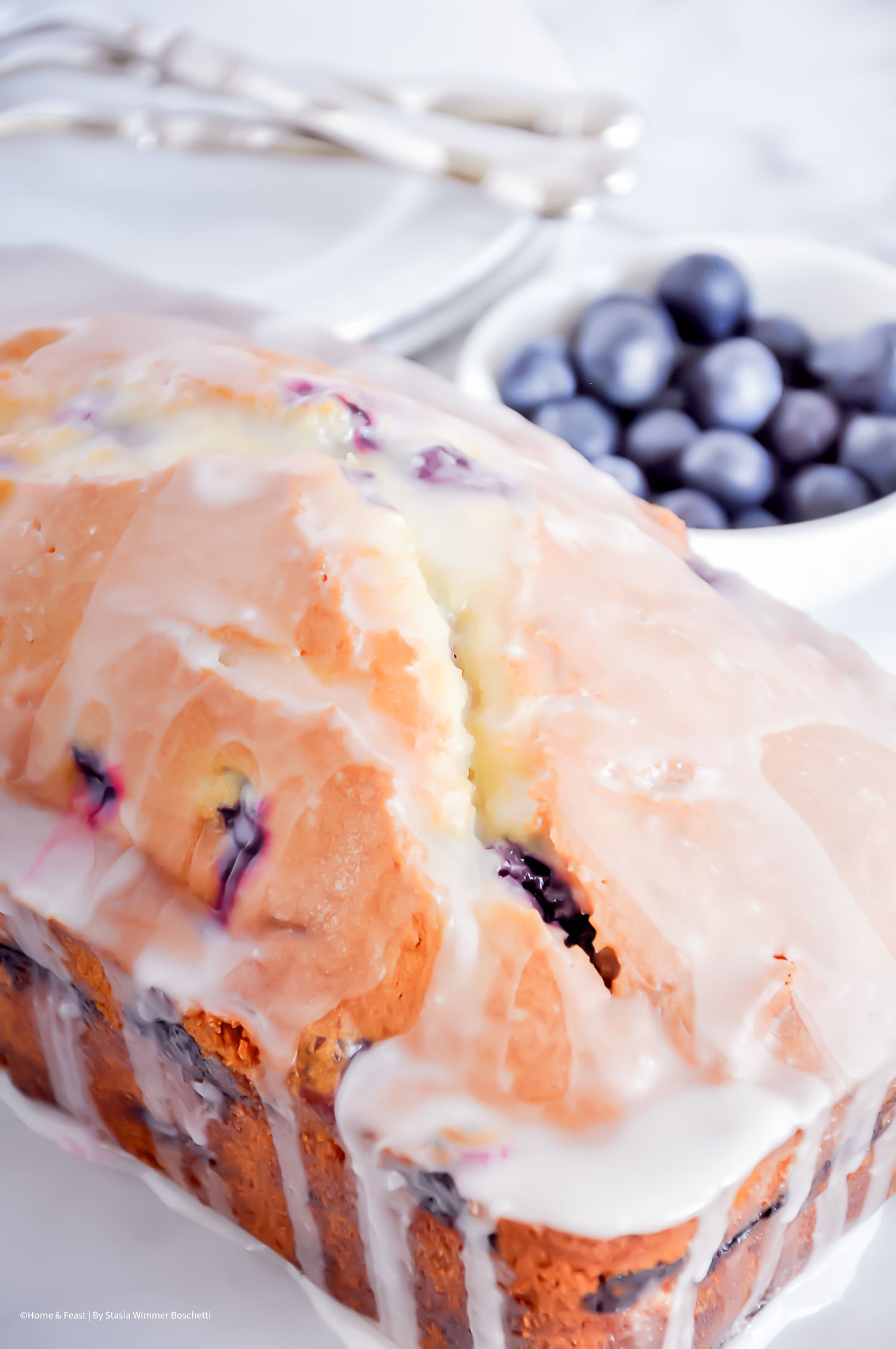 Glazed blueberry pound cake with white icing drizzle and fresh berries on the side.