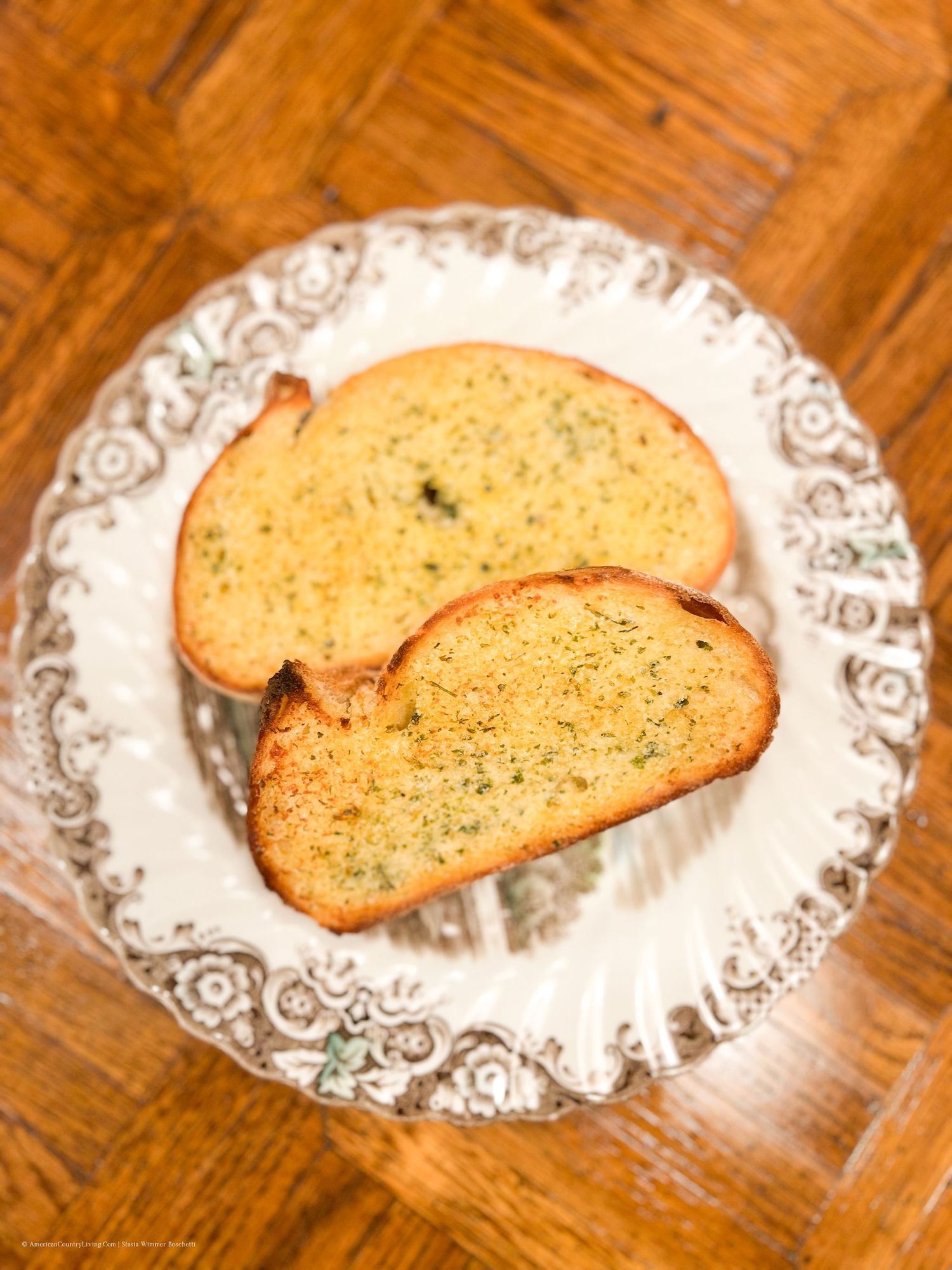 Crispy garlic bread slices arranged on decorative white plates with intricate border patterns.