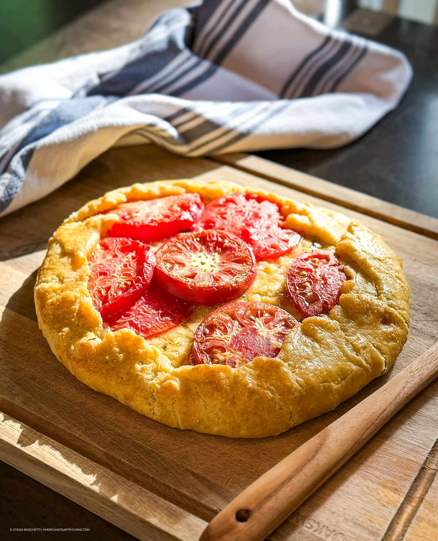 Rustic tomato galette with sliced heirloom tomatoes on golden pastry crust, served on a wooden cutting board.