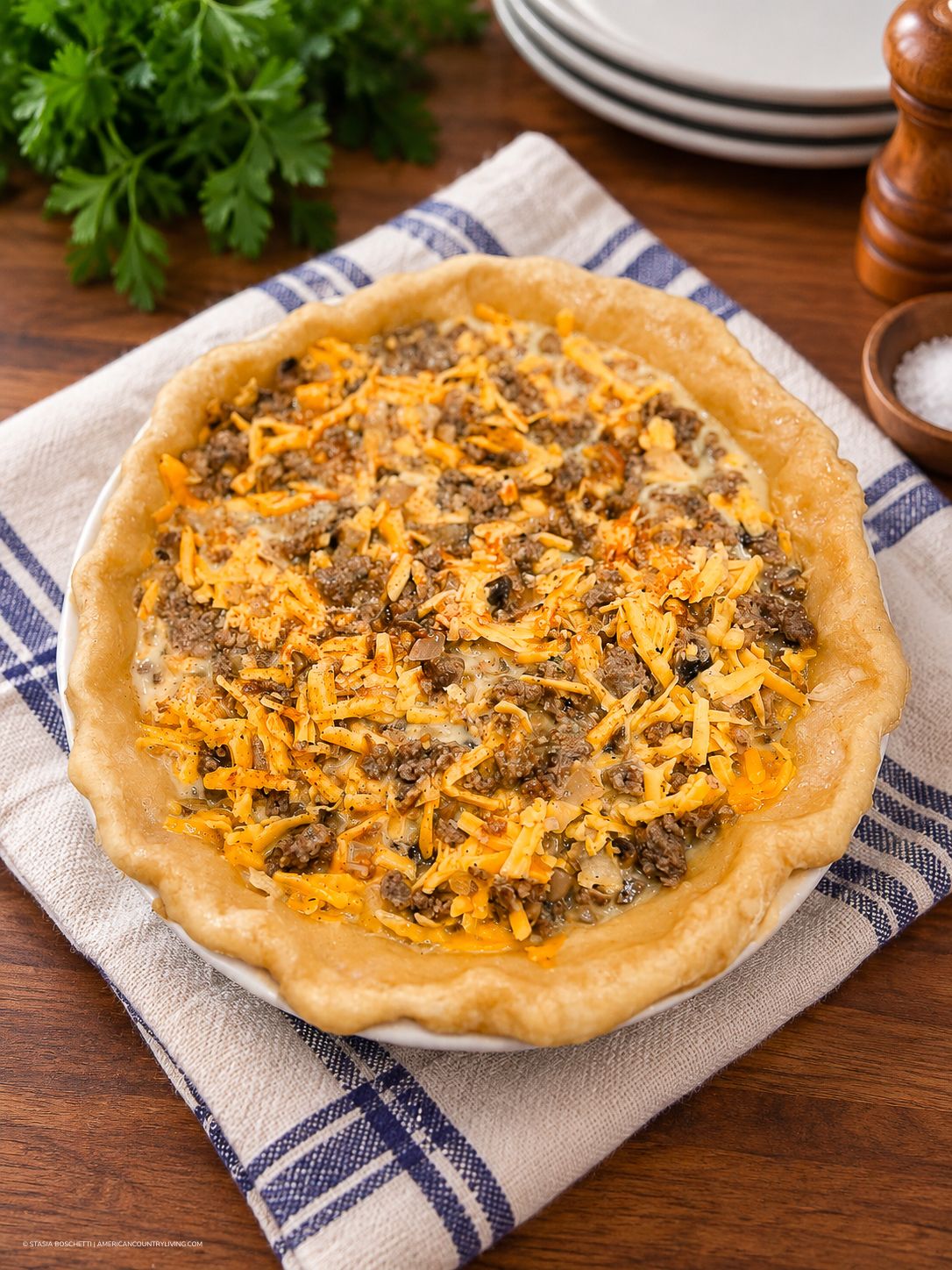 Savory ground beef and cheddar cheese pie in a golden flaky crust on a striped kitchen towel.