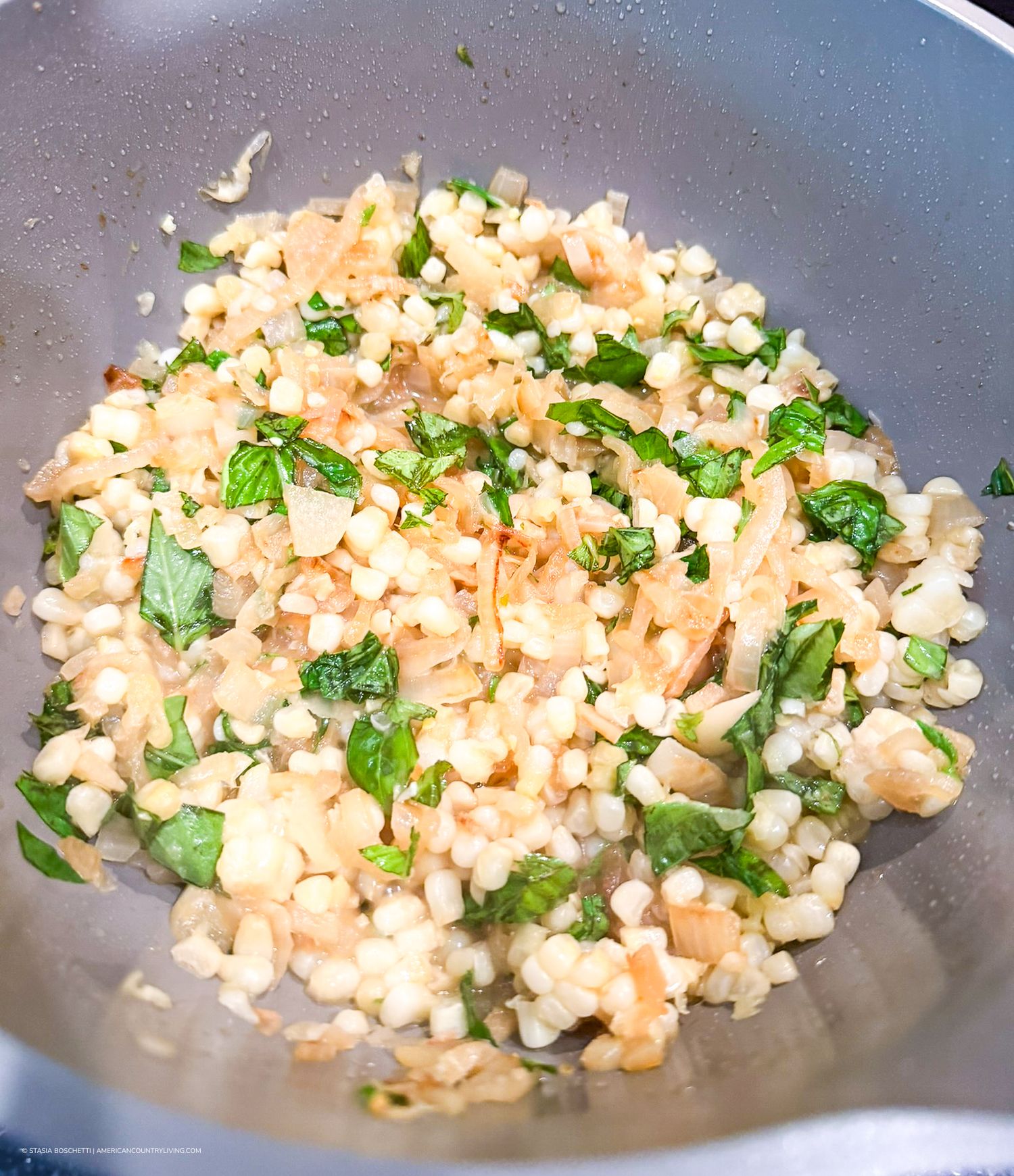 Sautéed pearl barley with fresh herbs and onions cooking in a wok, a healthy grain dish.