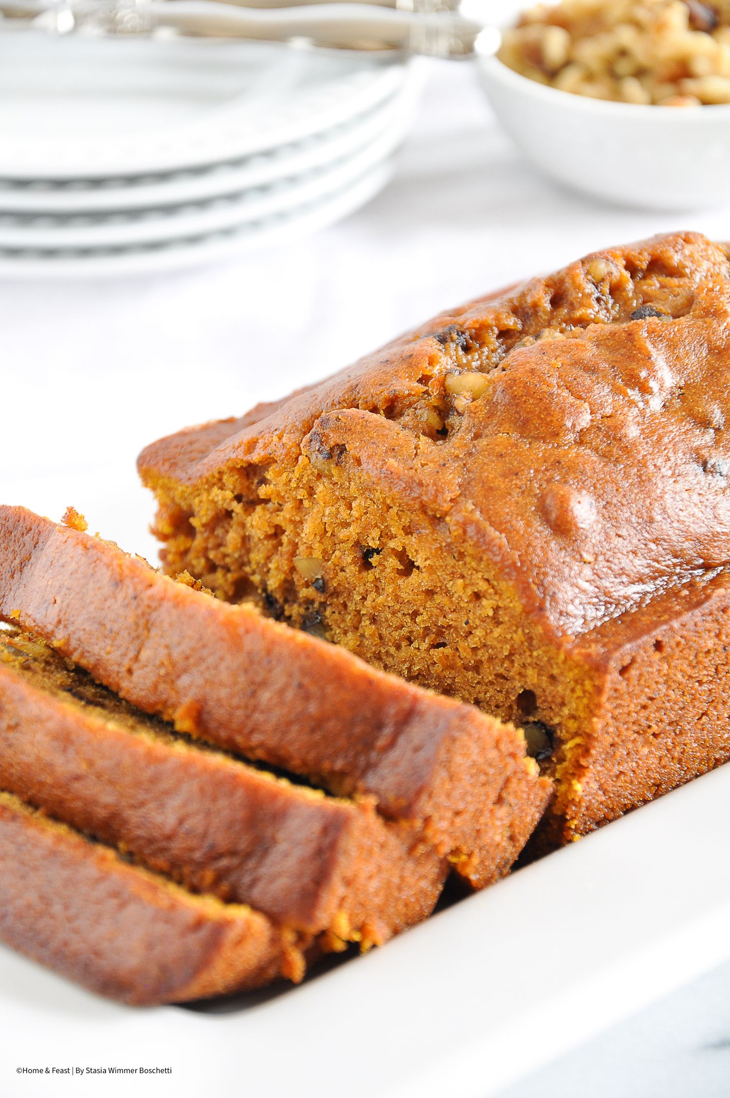 Sliced pumpkin bread with golden brown crust displayed on white serving platter.