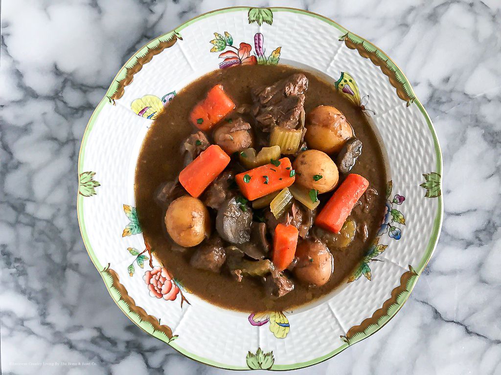 Homemade beef stew with carrots and potatoes served on decorative plates with floral trim.